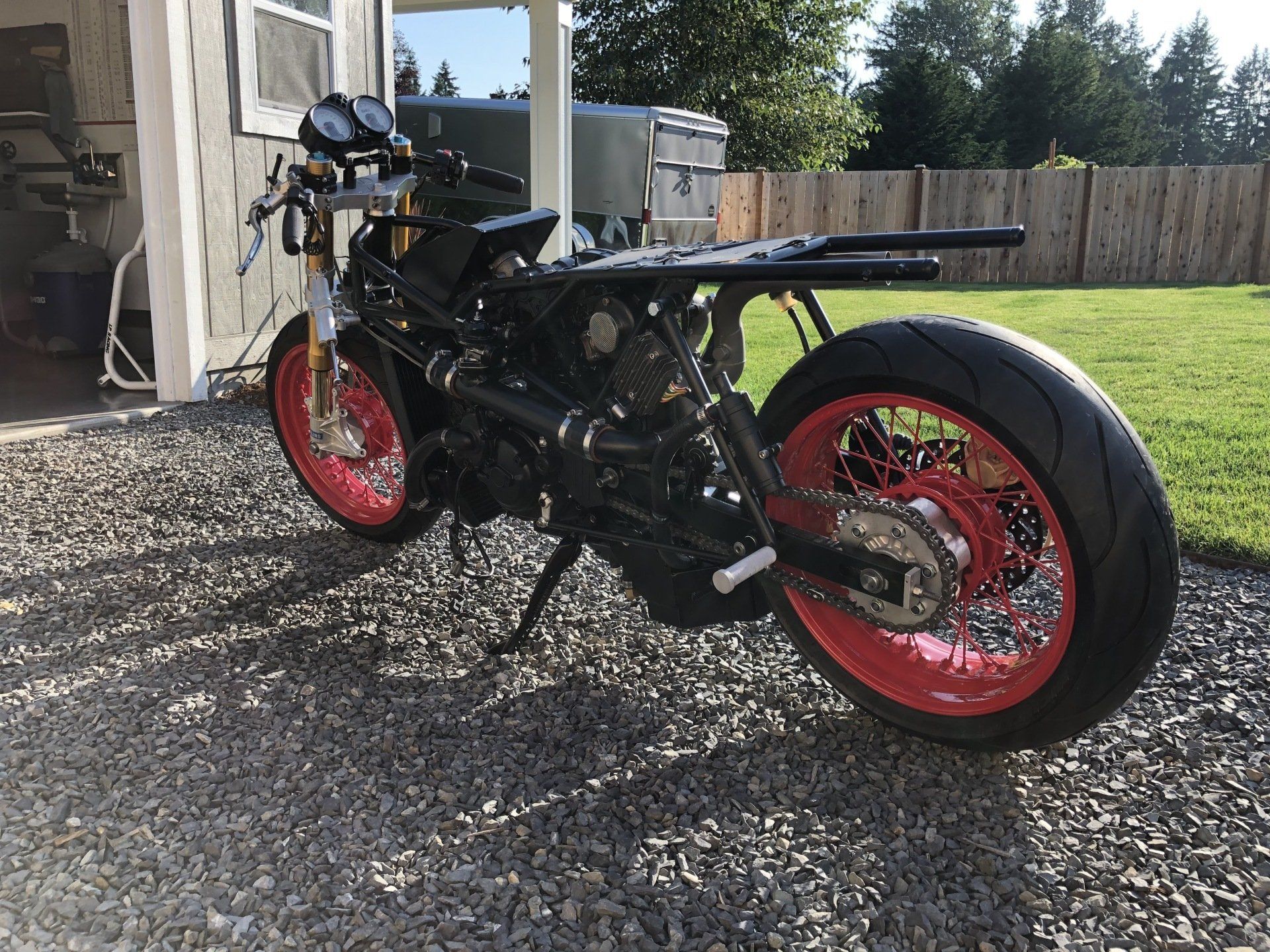 A black motorcycle with red wheels is parked in a gravel driveway.