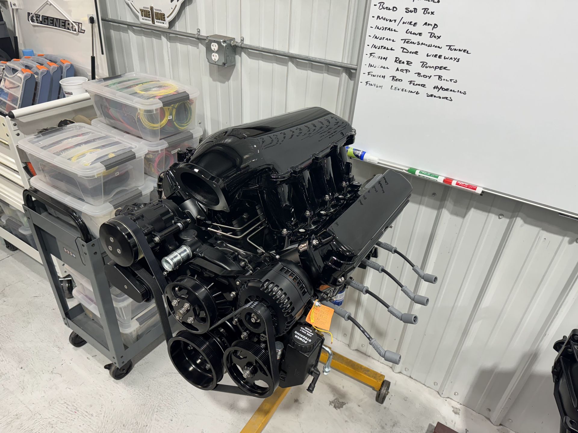 A black engine is sitting on a stand in a garage next to a white board.