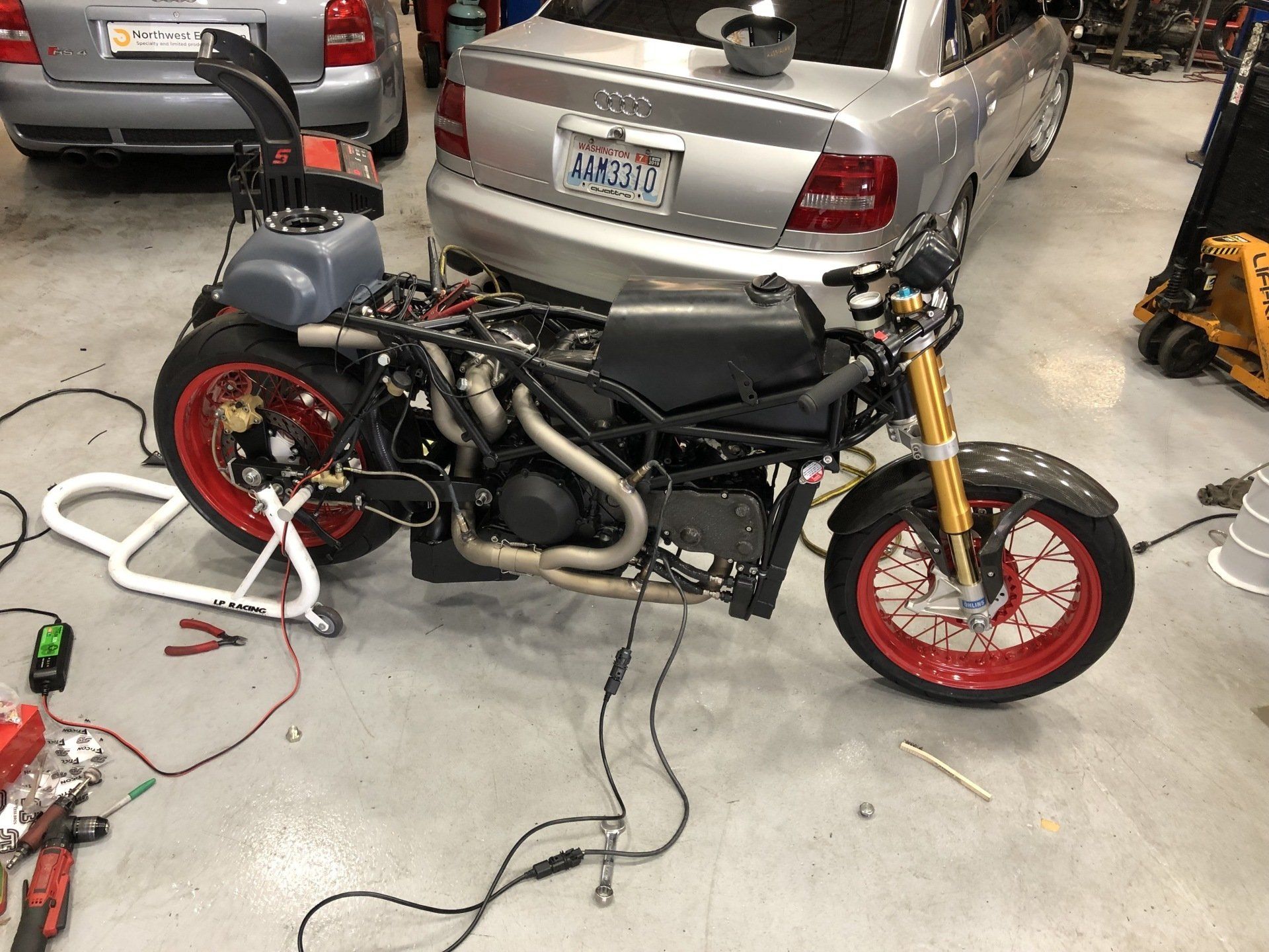 A motorcycle is being worked on in a garage next to a car.