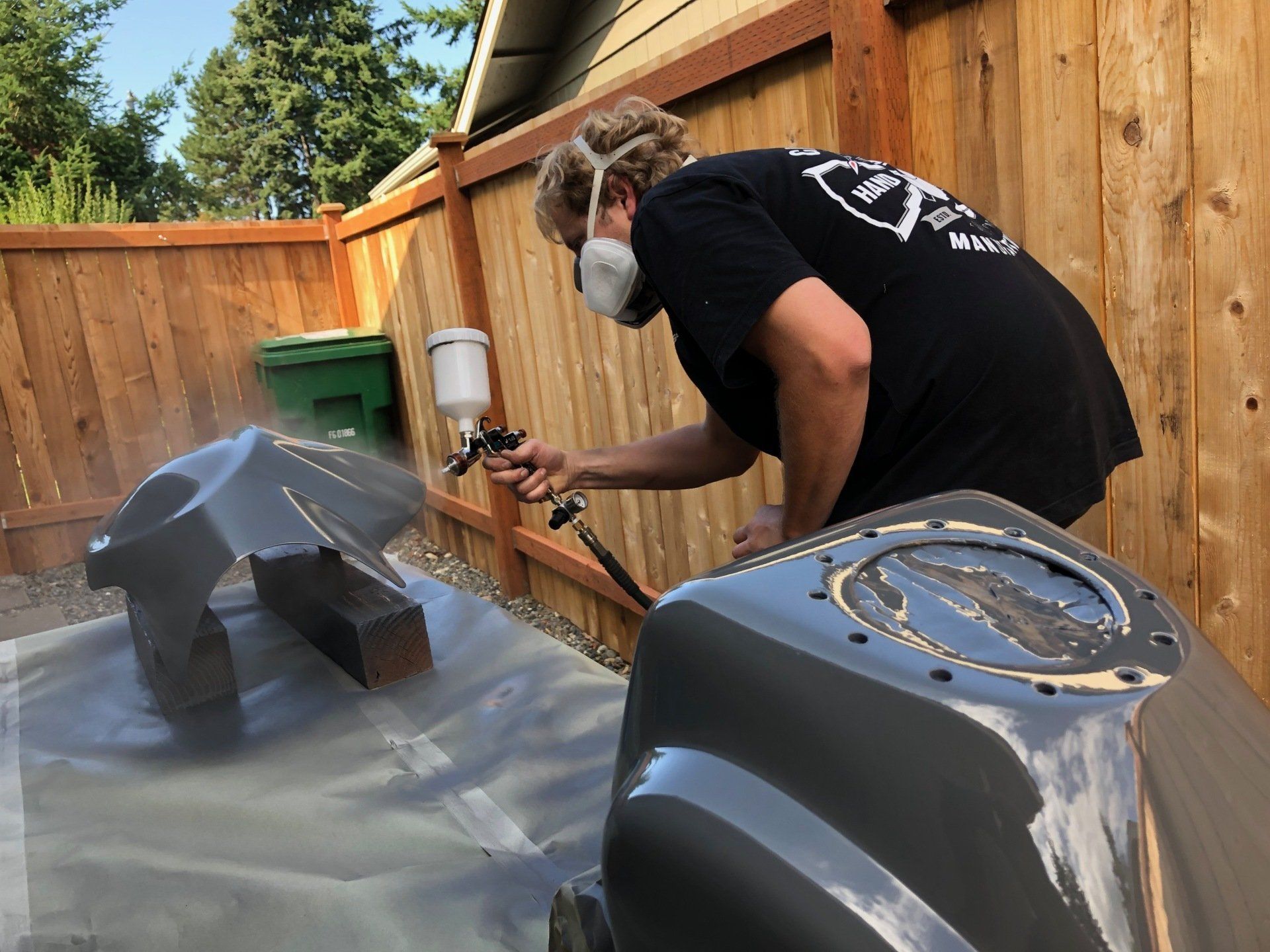 A man wearing a mask is spray painting a motorcycle