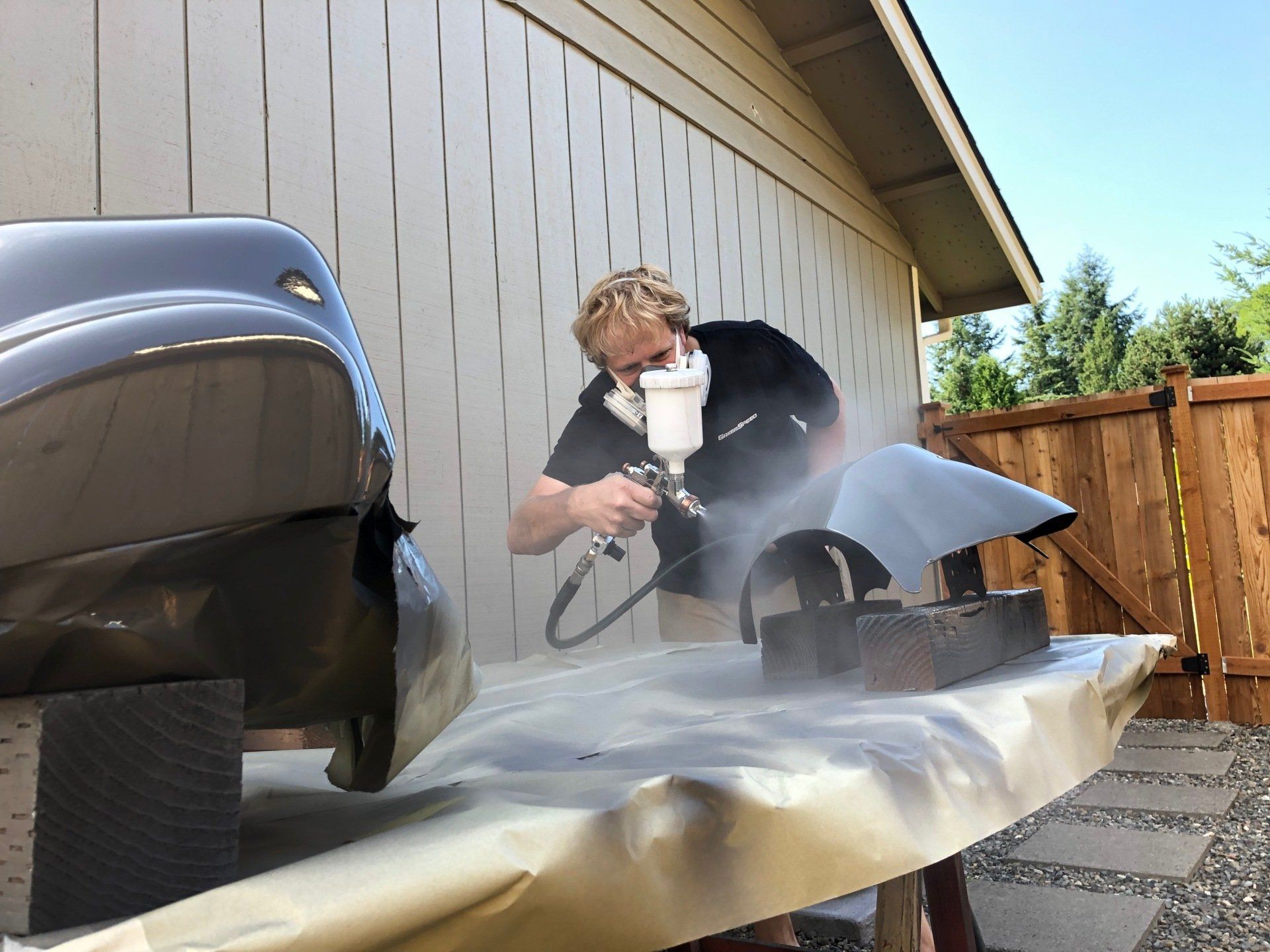 A man wearing a mask is spray painting a car