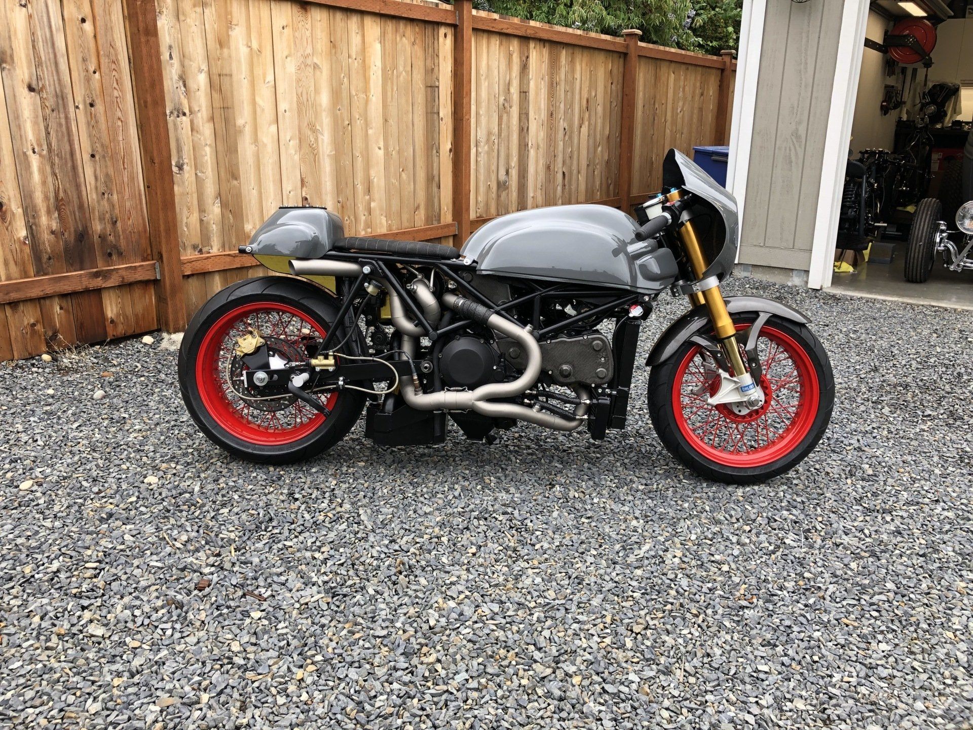 A motorcycle is parked in a gravel lot next to a wooden fence.