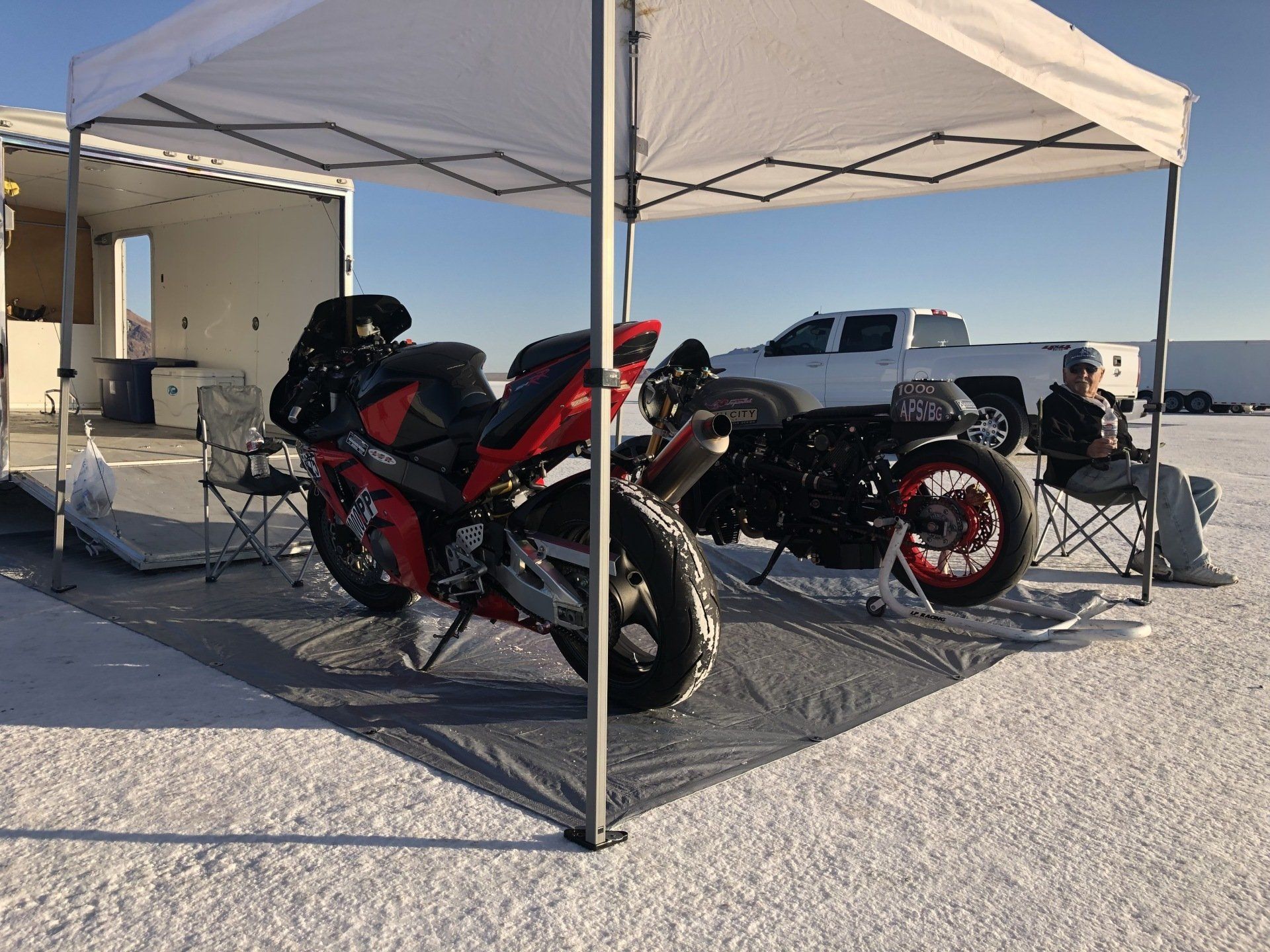 Two motorcycles are parked under a tent in the snow.