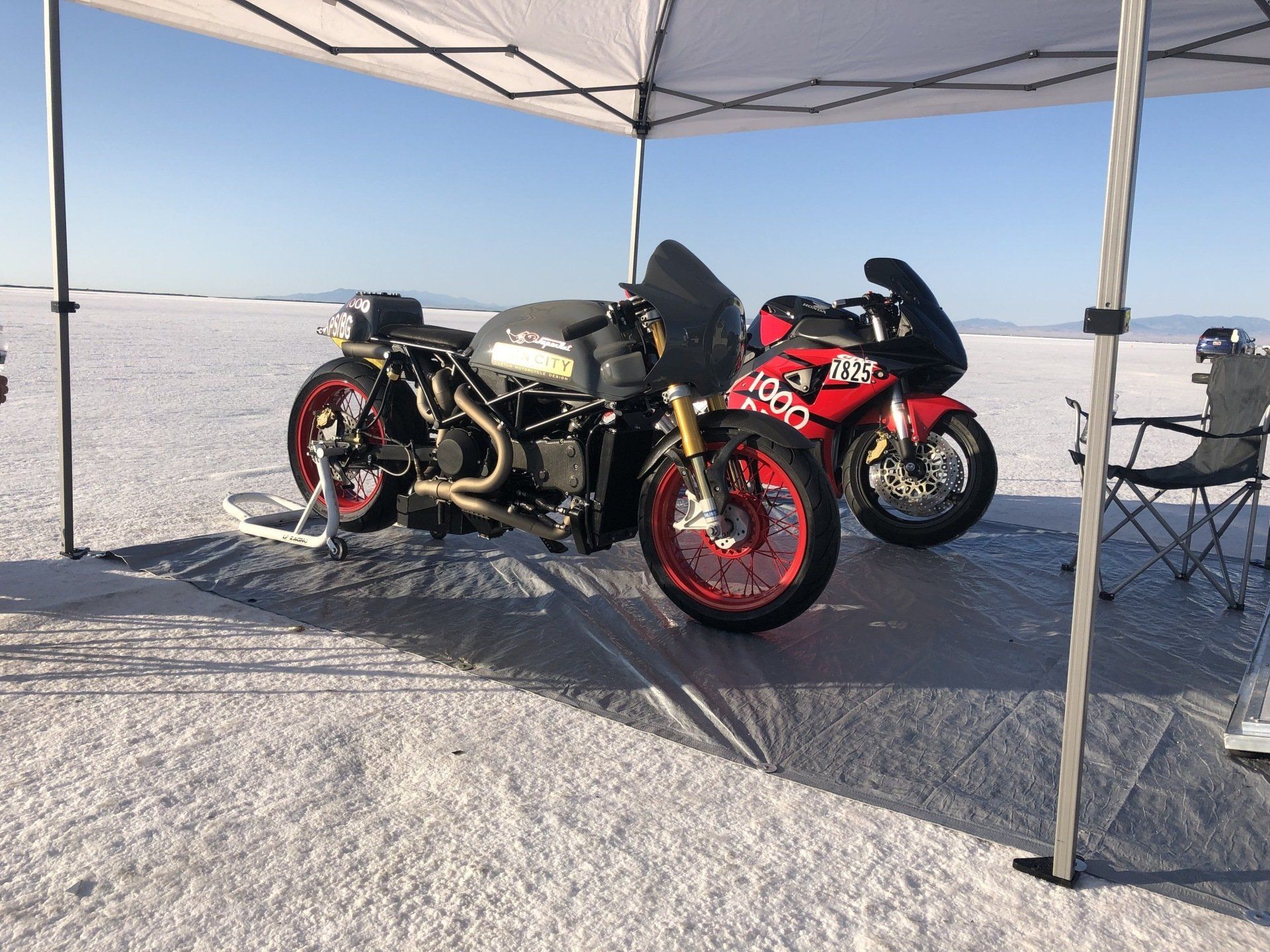 Two motorcycles are parked under a tent on a snowy field.