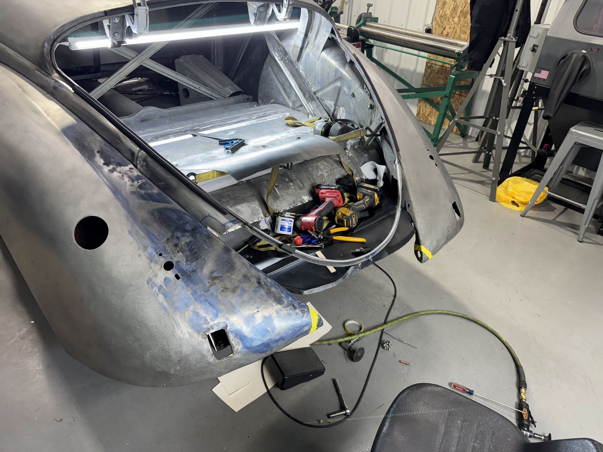 A car is being worked on in a garage with the trunk open.