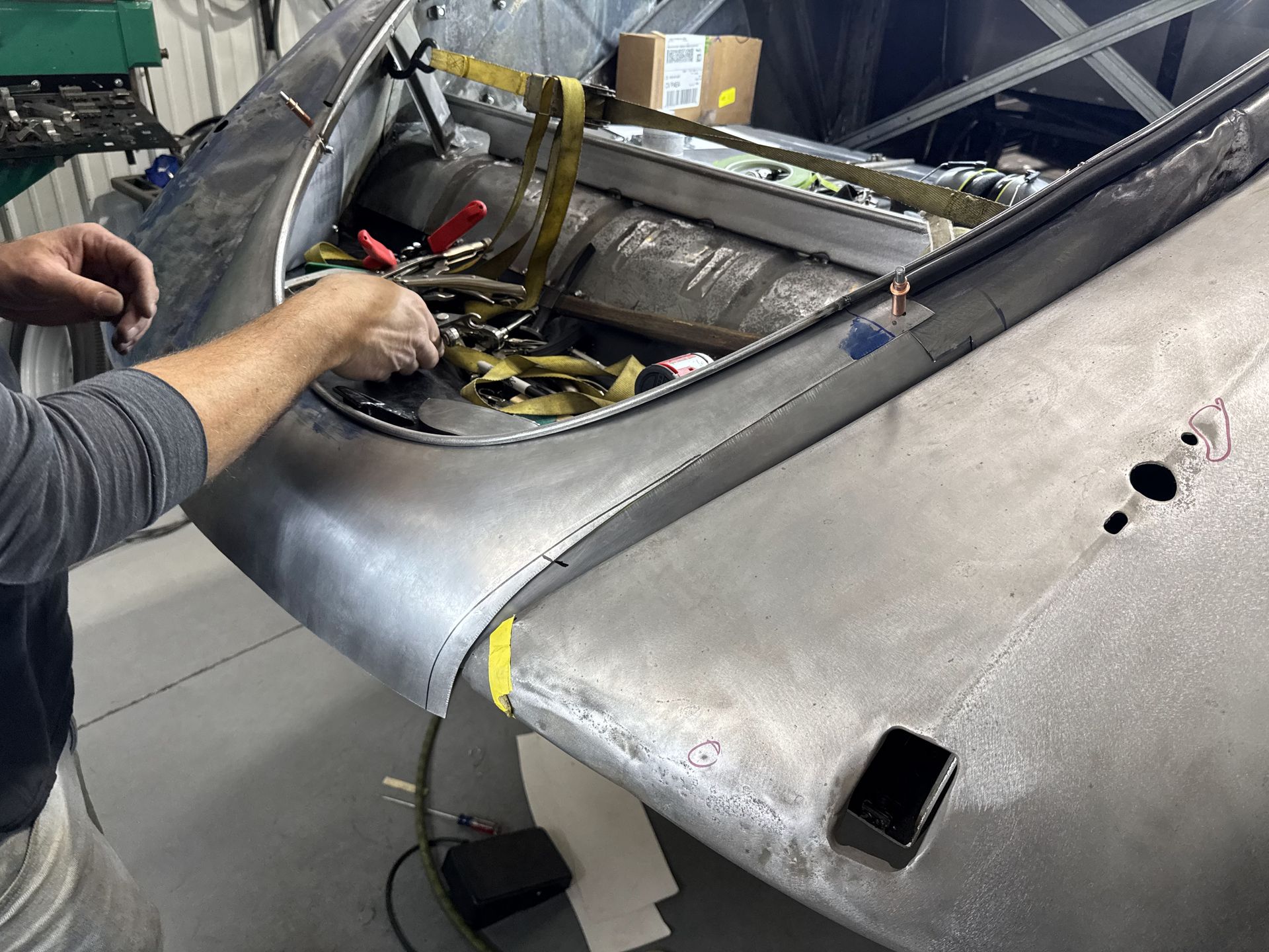 A man is working on the hood of a car in a garage.