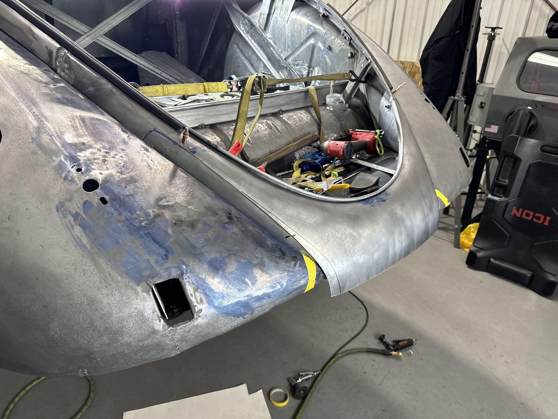 A car is being worked on in a garage with the hood open.
