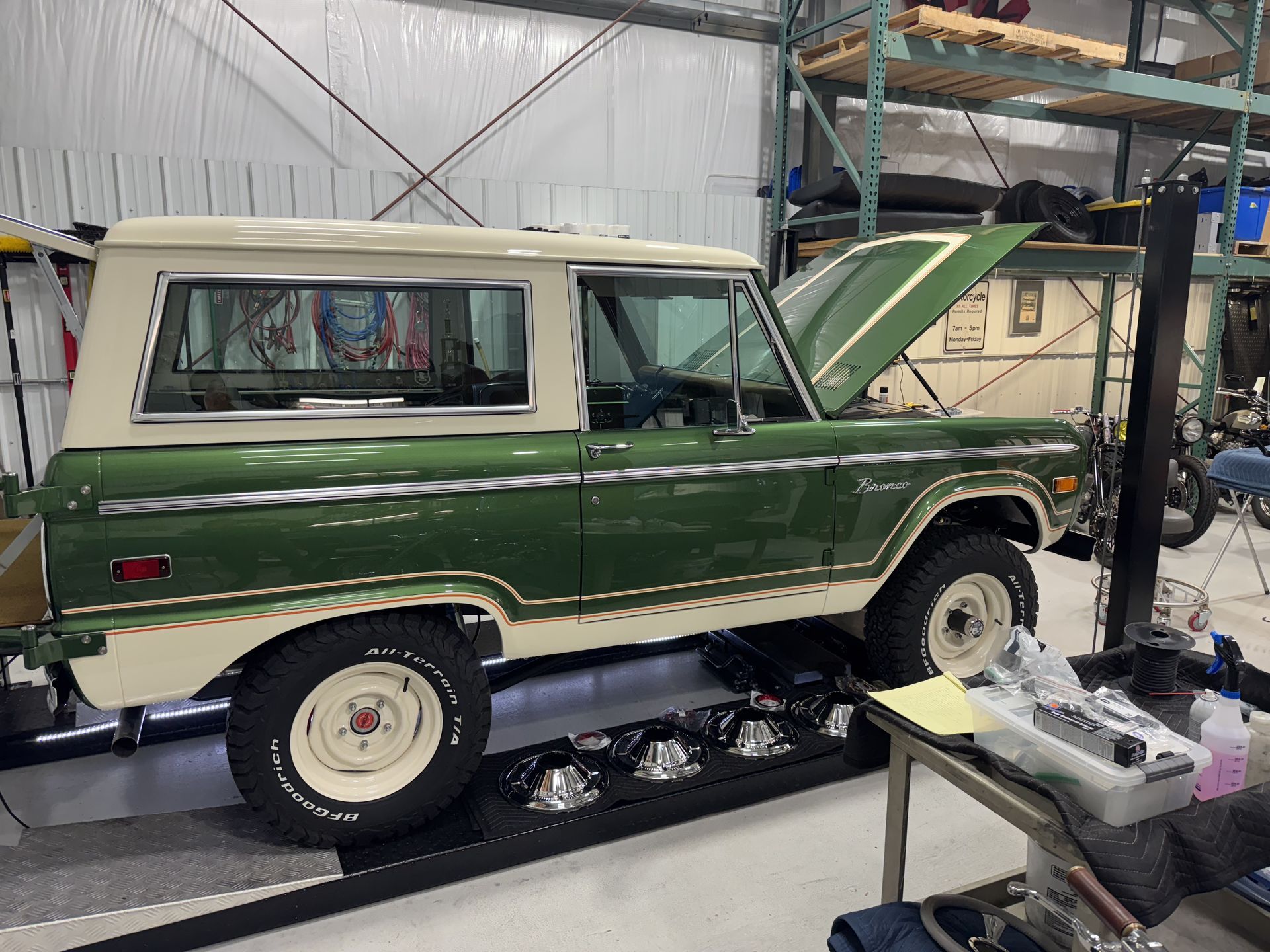 A green and white ford bronco is parked in a garage with its hood up.