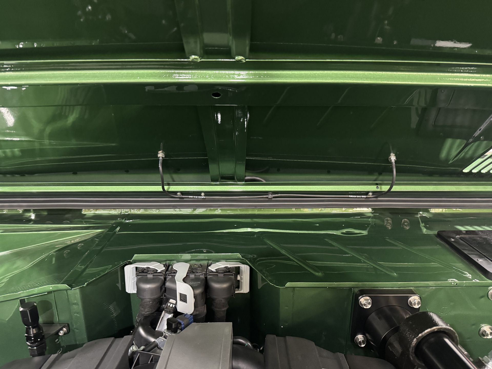 The hood of a green car is open and shows the engine.