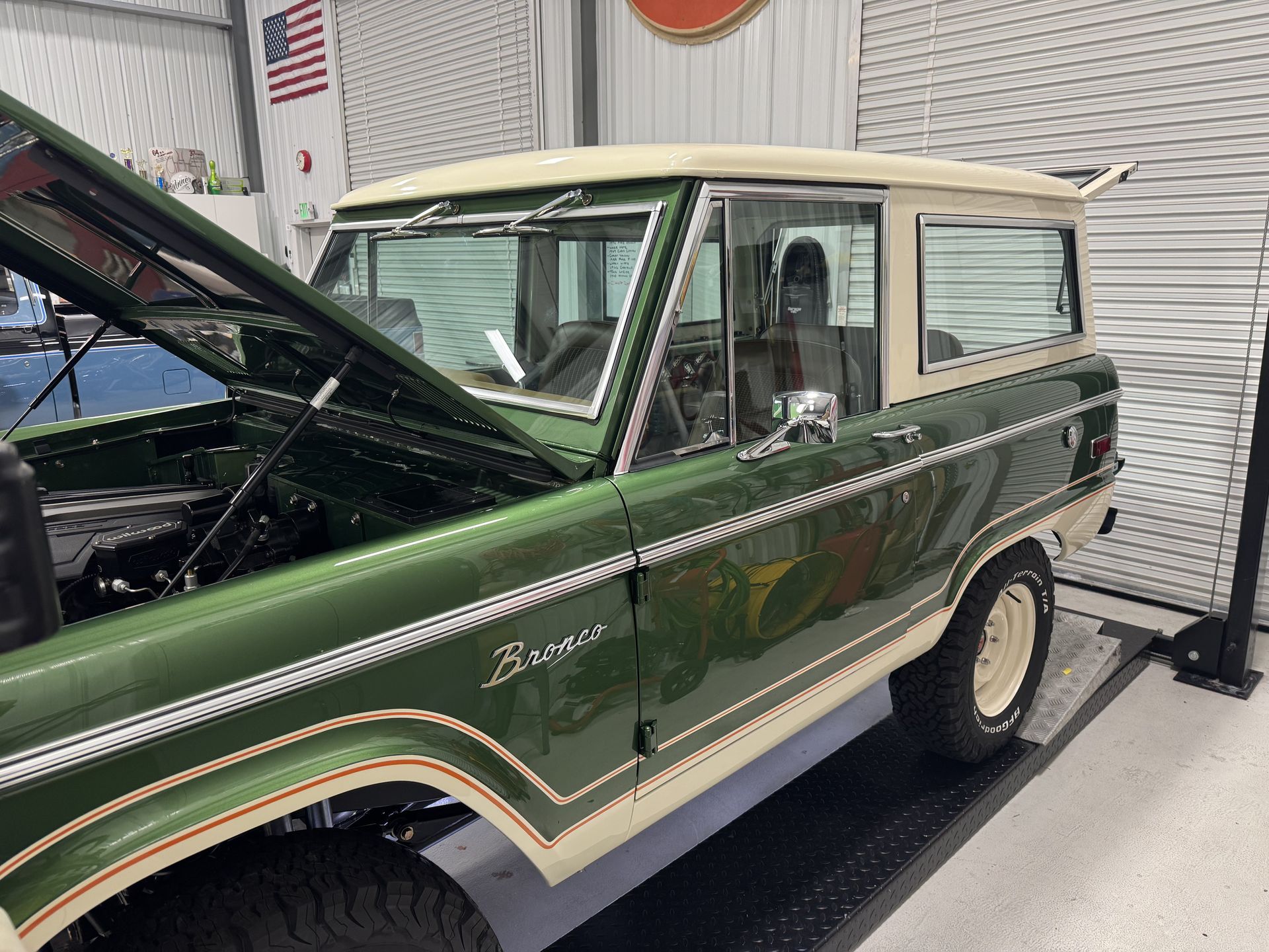 A green and white jeep with the hood up is parked in a garage.