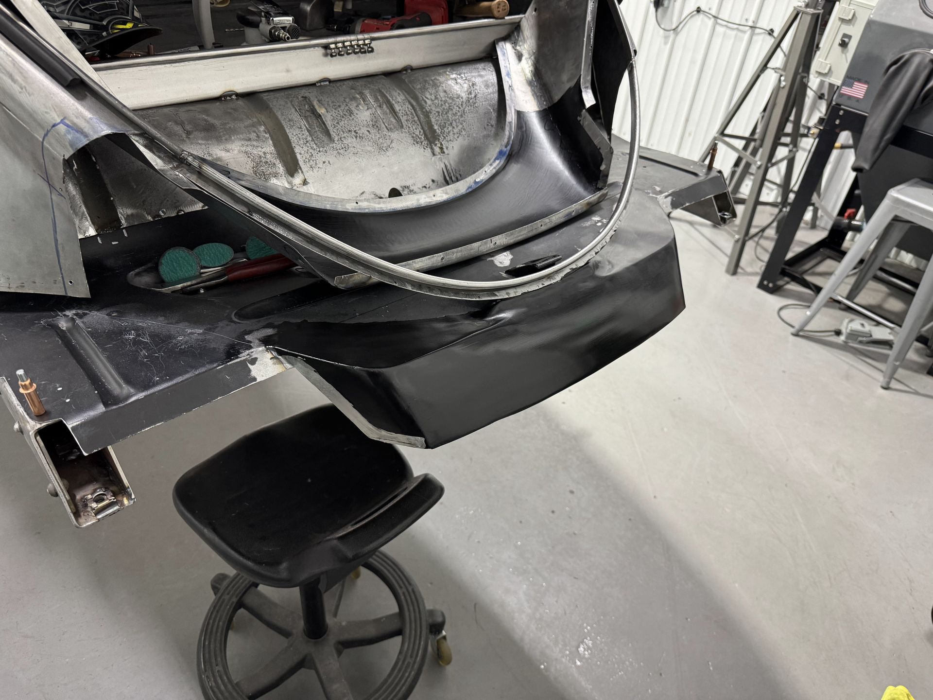 A car is being worked on in a garage with a stool in front of it