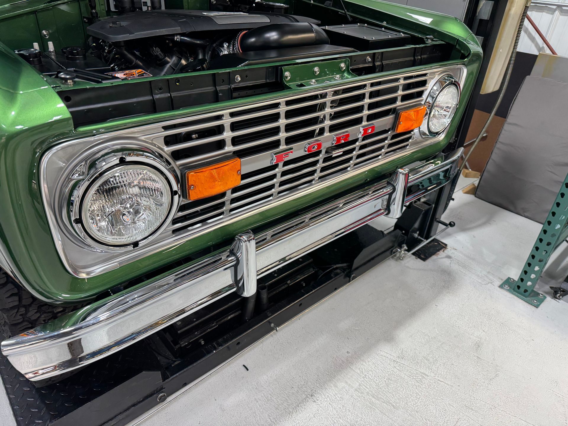 A green ford bronco is parked in a garage with the hood open.