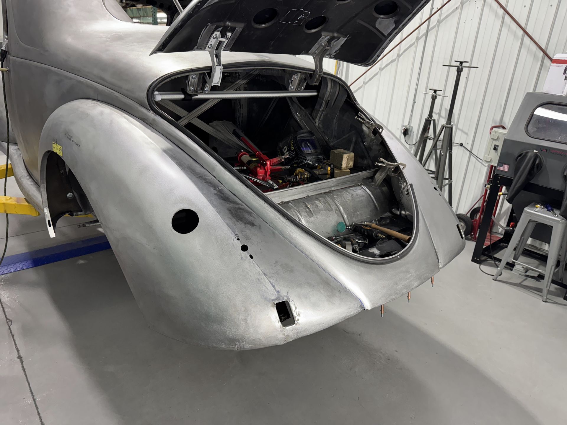 A silver car with the hood open is sitting in a garage.