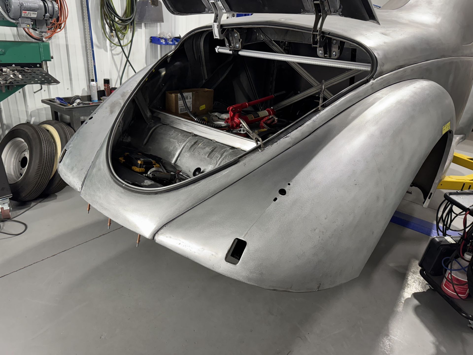 A silver car with the trunk open is sitting in a garage.