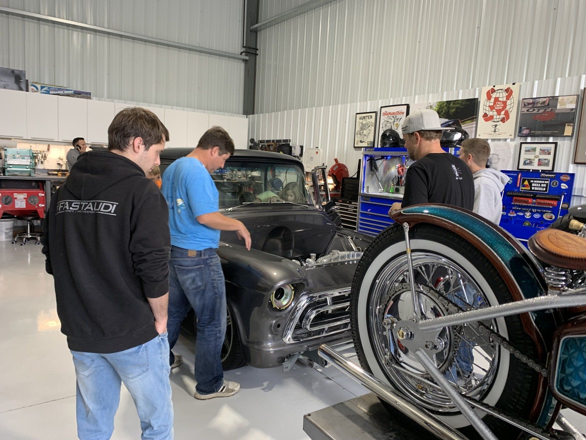 A group of men are looking at a car and a motorcycle in a garage.