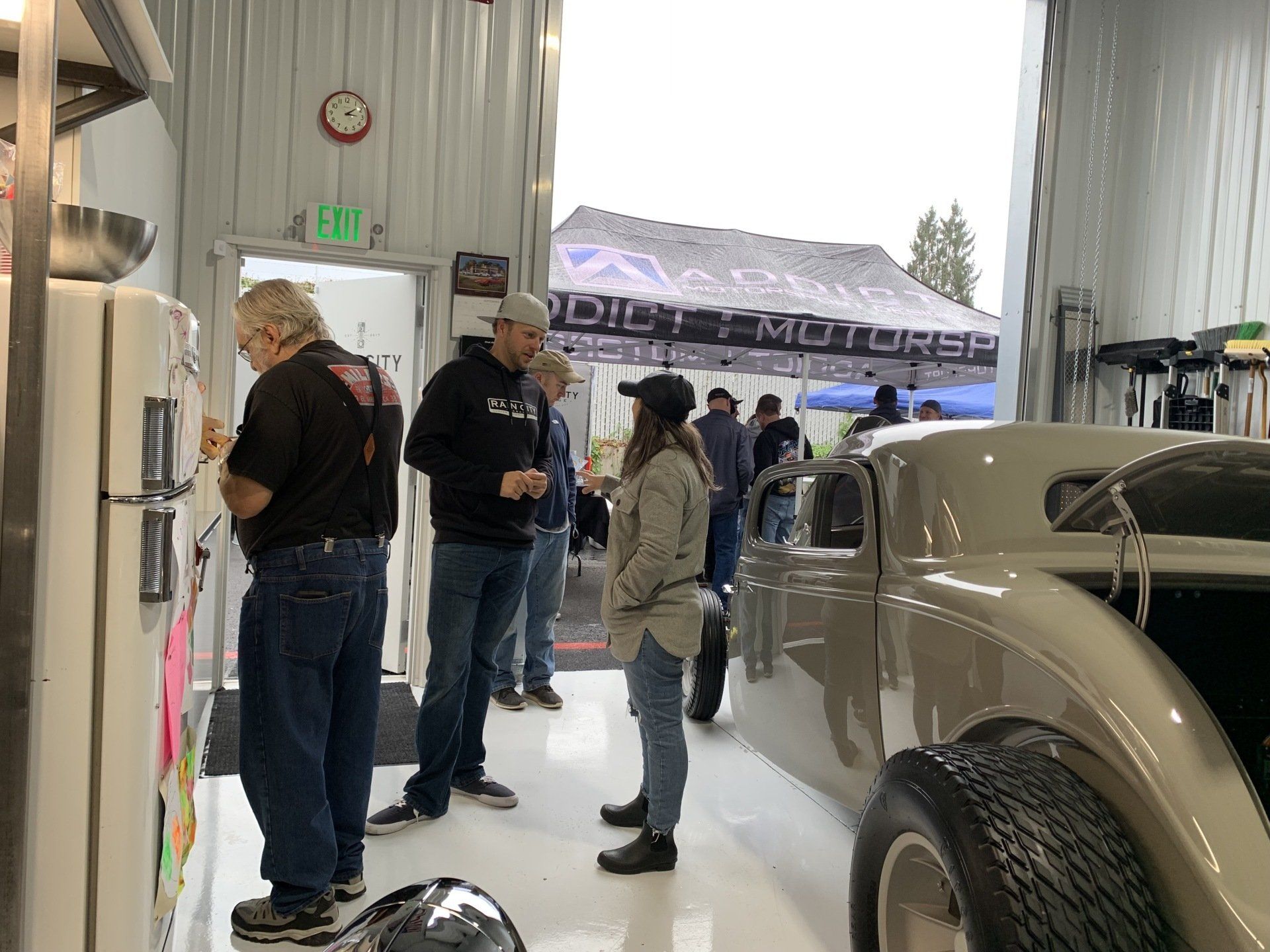 A group of people are standing around a car in a garage.