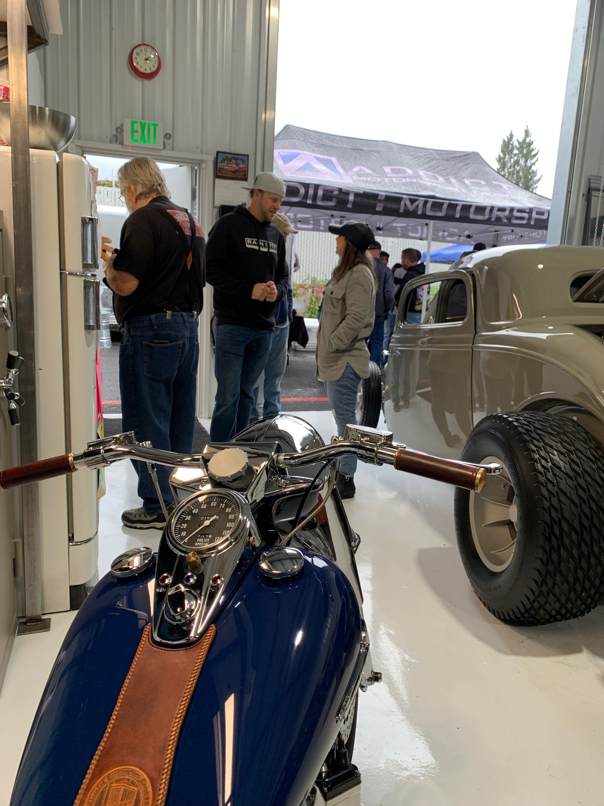 A group of people are standing around a motorcycle in a garage with an exit sign in the background