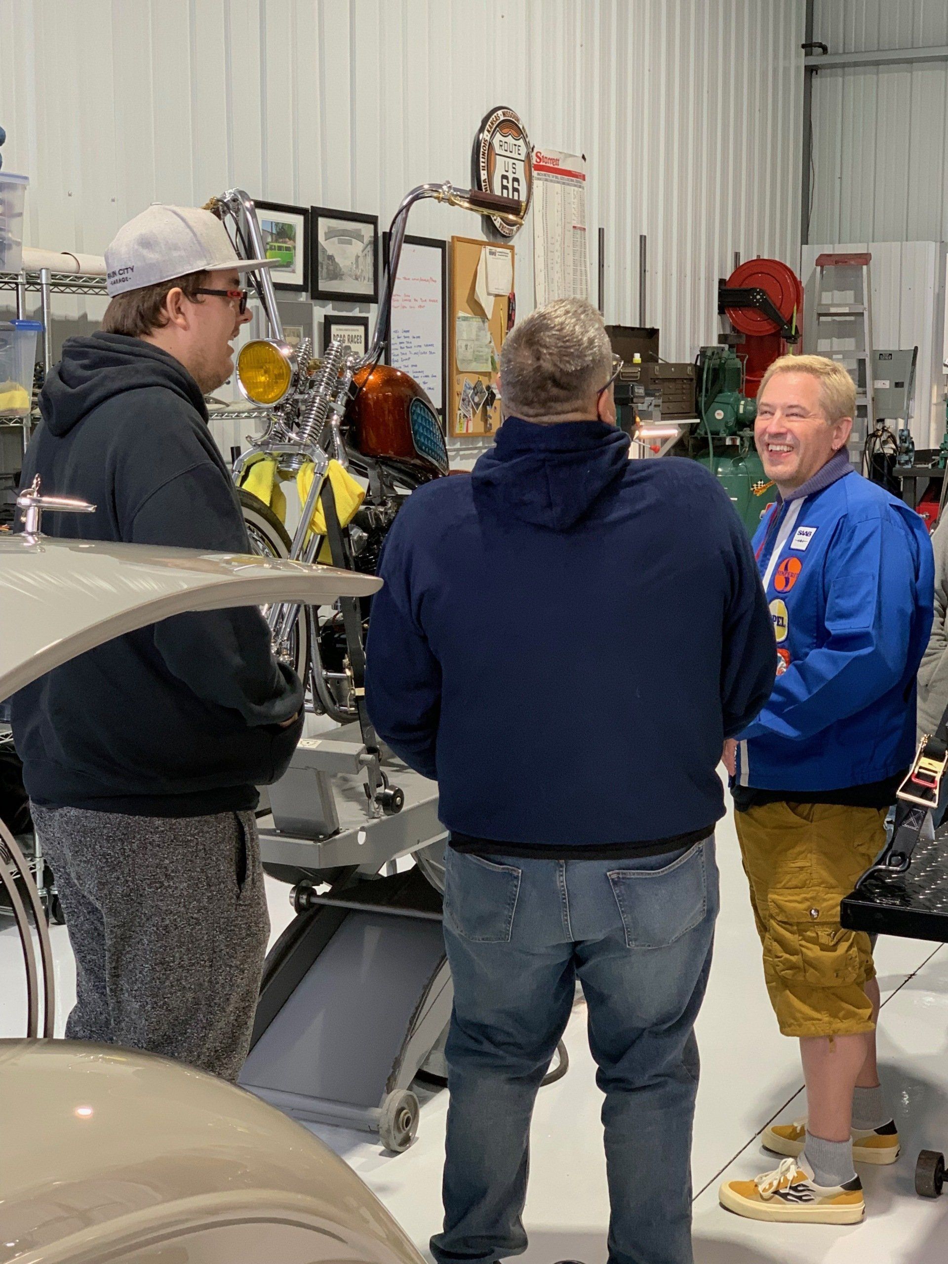 A group of men are standing in a garage talking to each other.