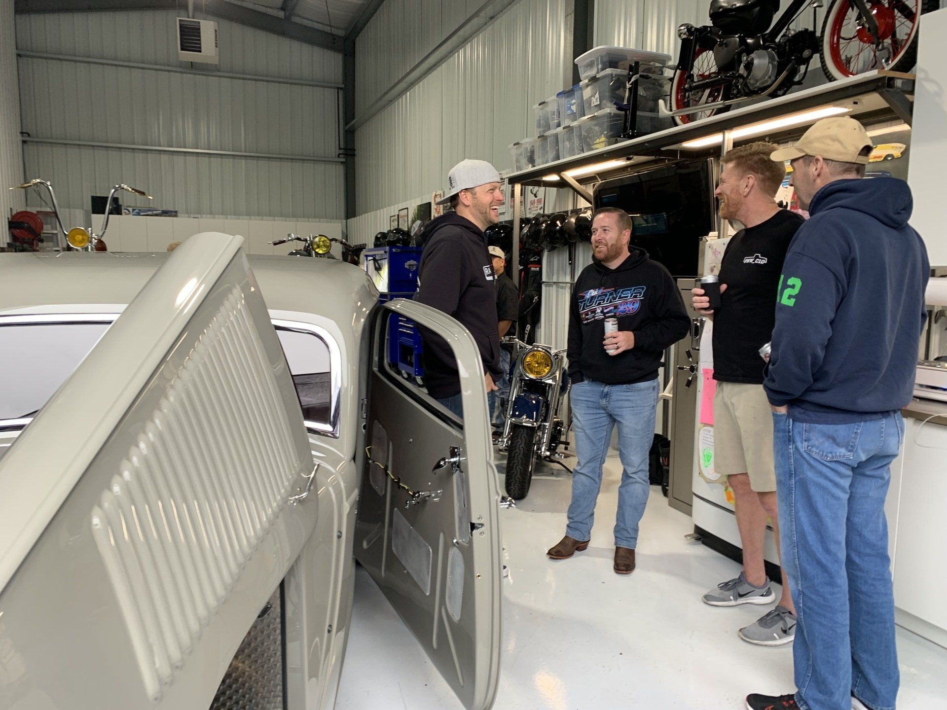 A group of men are standing around a car in a garage.