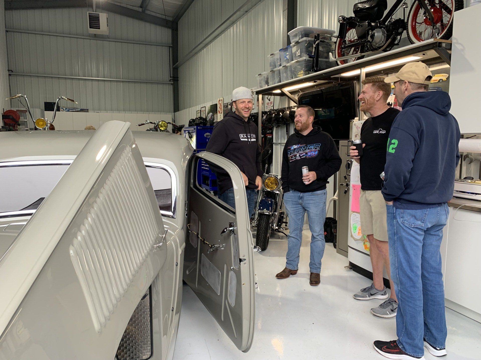 A group of men are standing around a car in a garage.