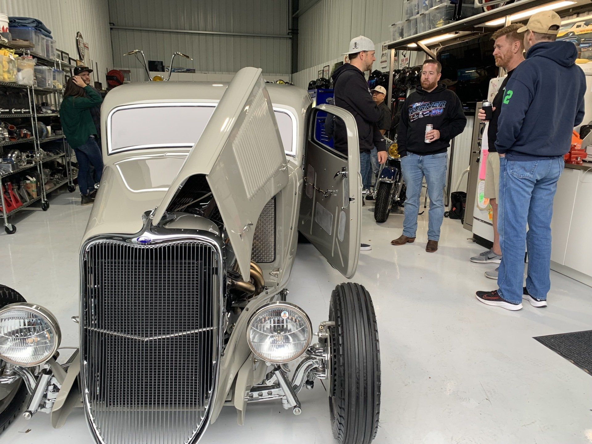 A group of men are standing around a car in a garage.