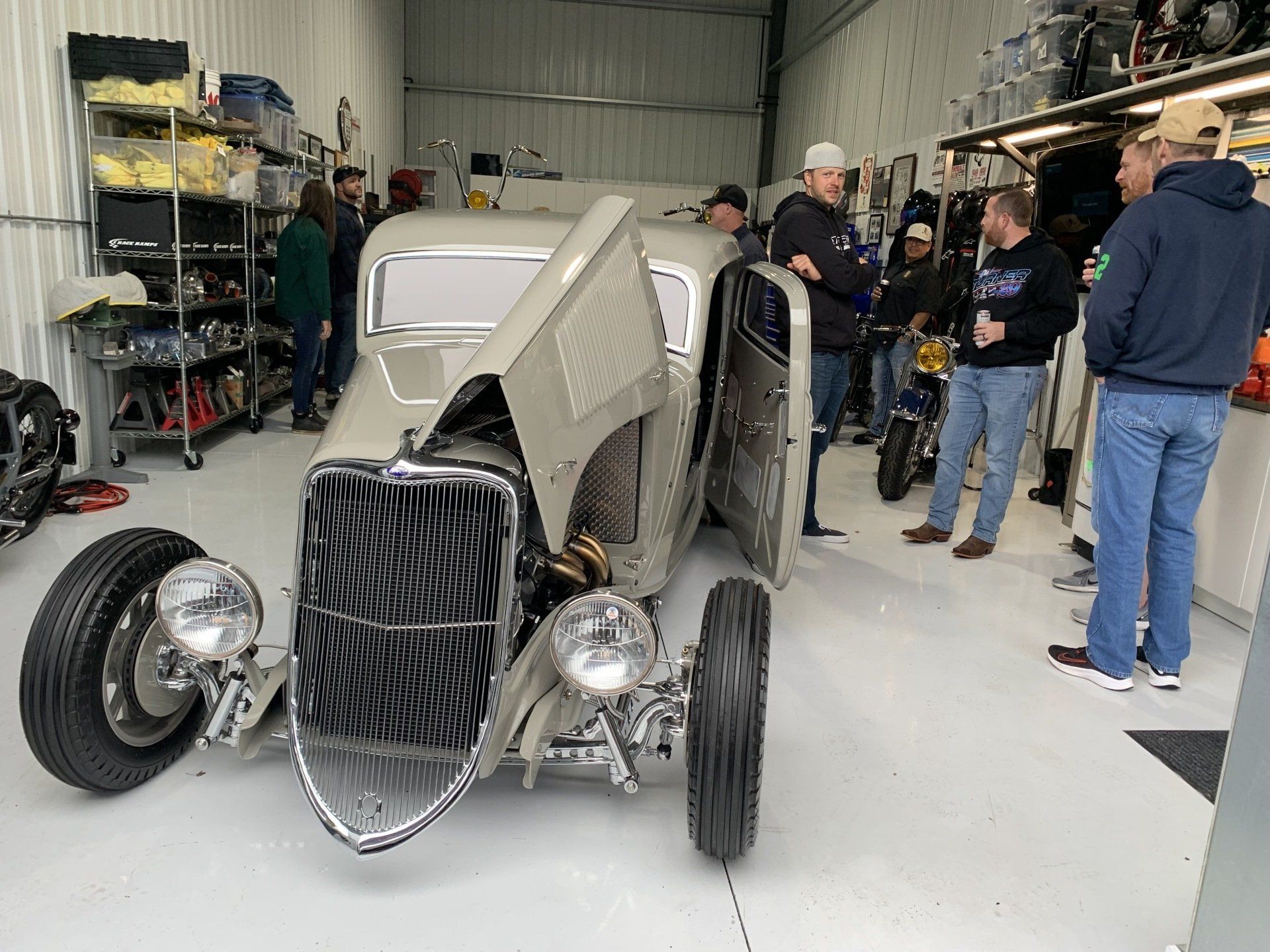 A group of men are standing around a car in a garage.