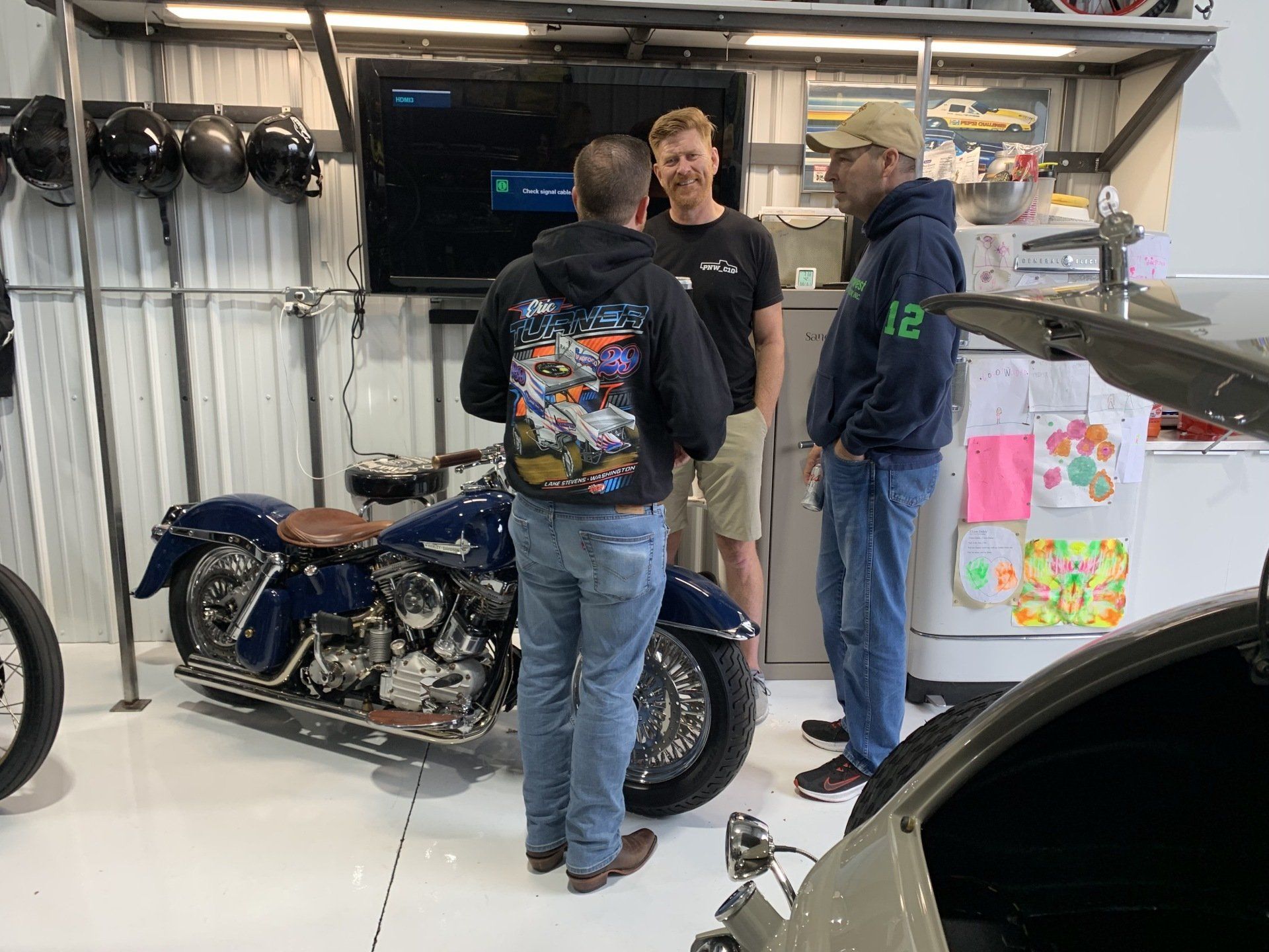 Three men are standing in front of a motorcycle in a garage.
