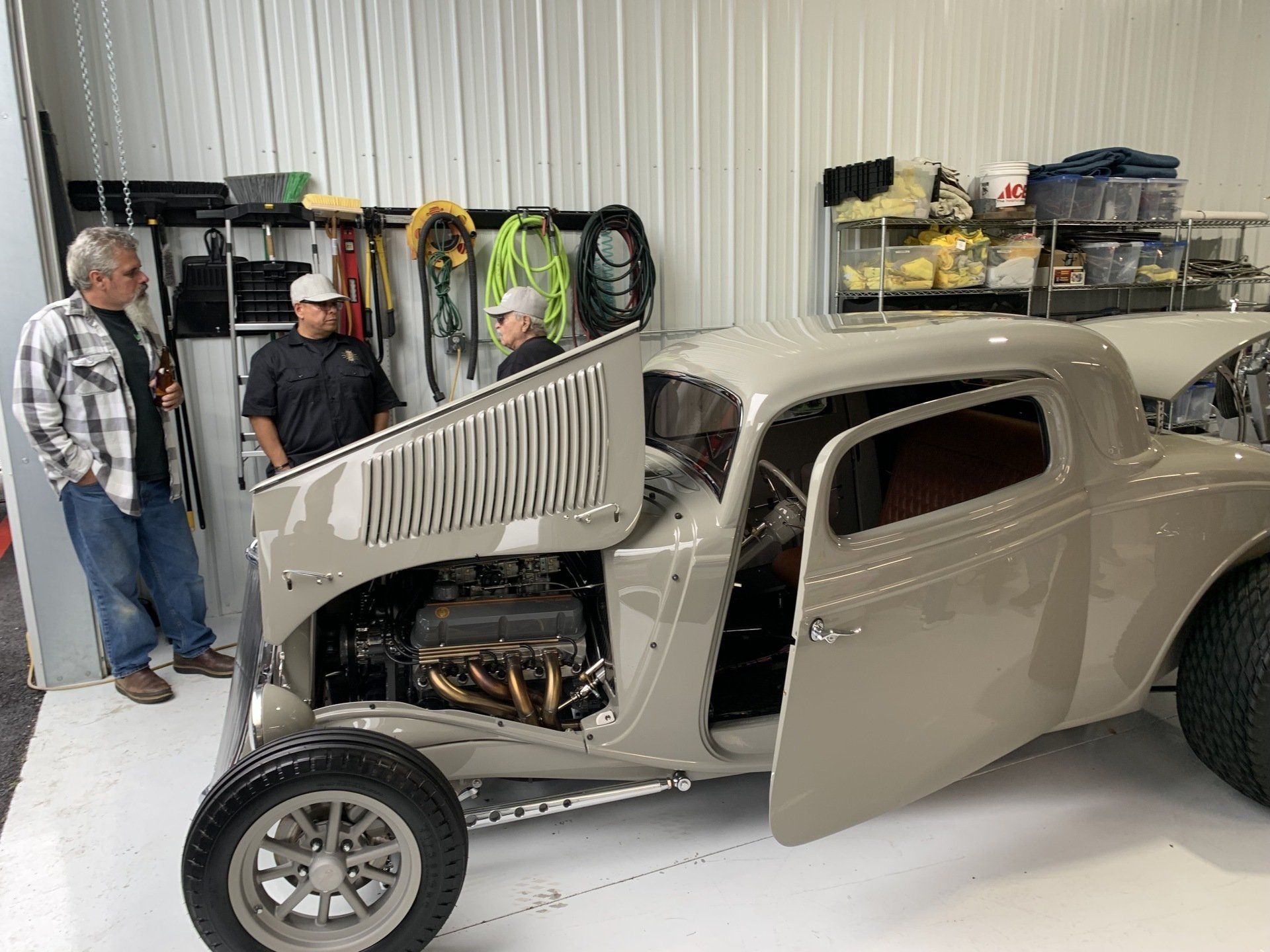 A man is standing next to a car with the hood open in a garage.