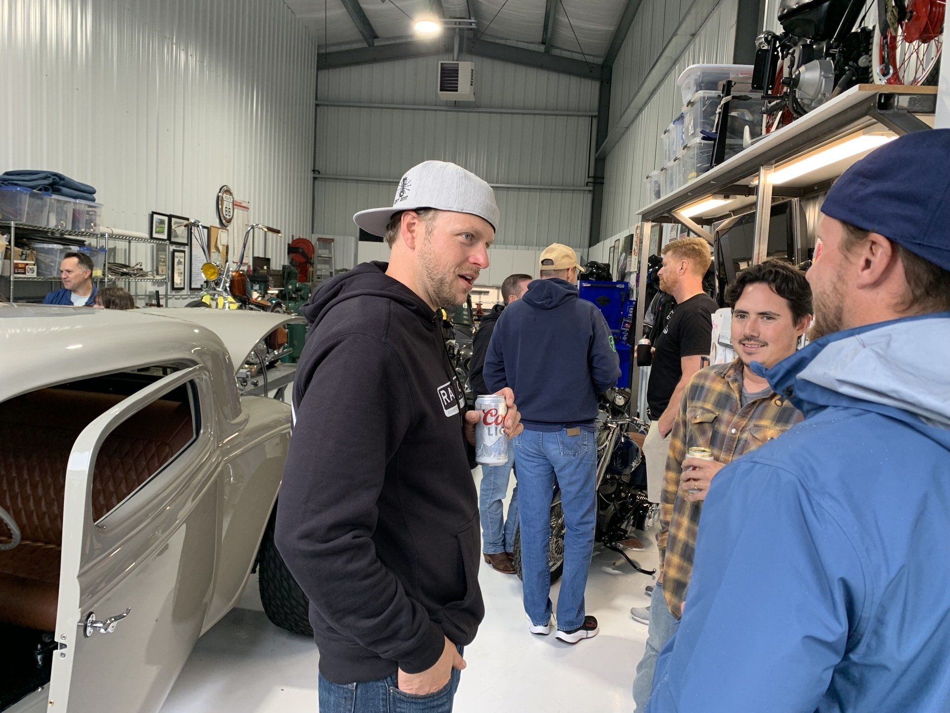 A group of men are standing in a garage talking to each other.