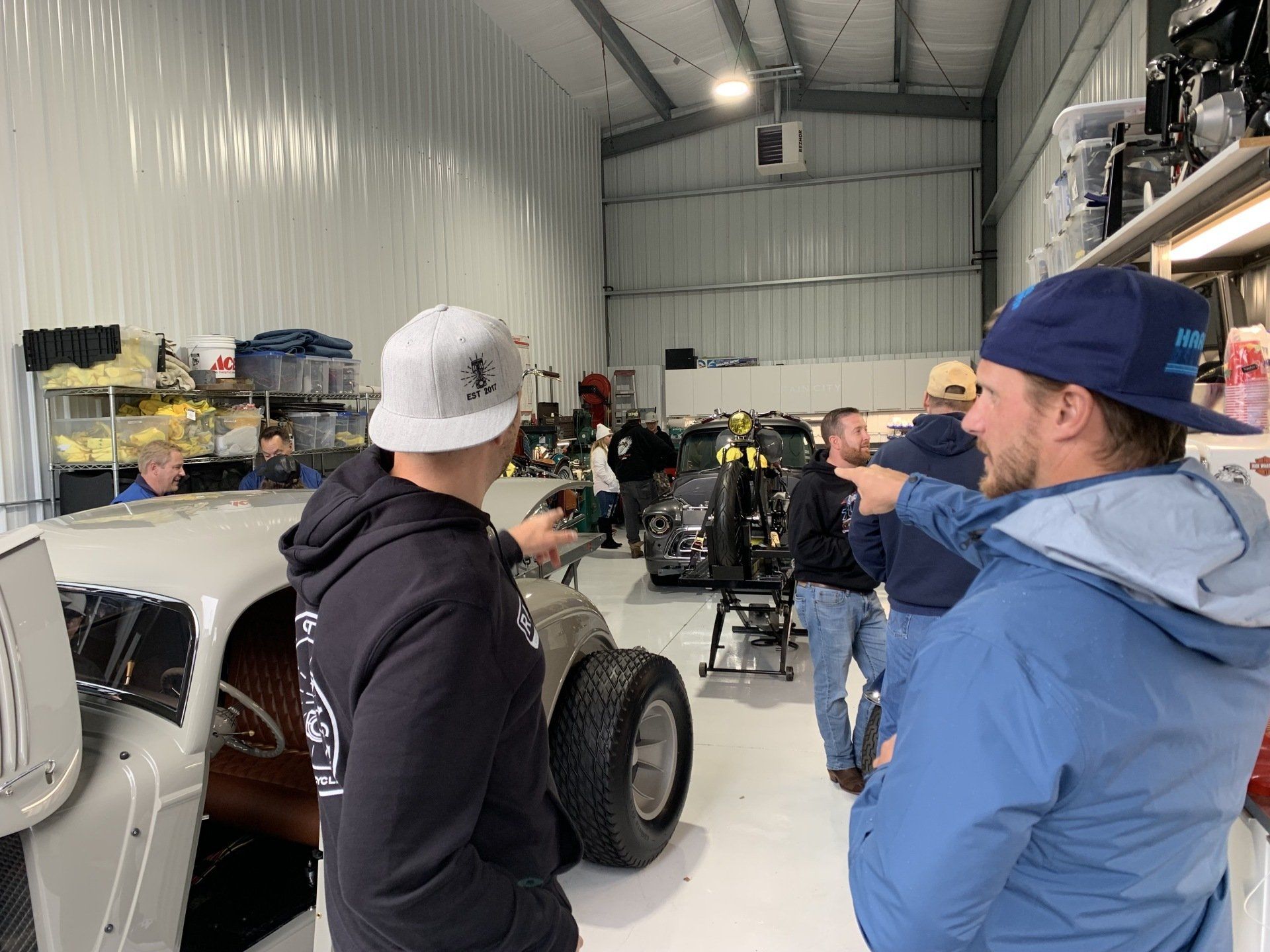 A group of men are standing in a garage looking at a car.