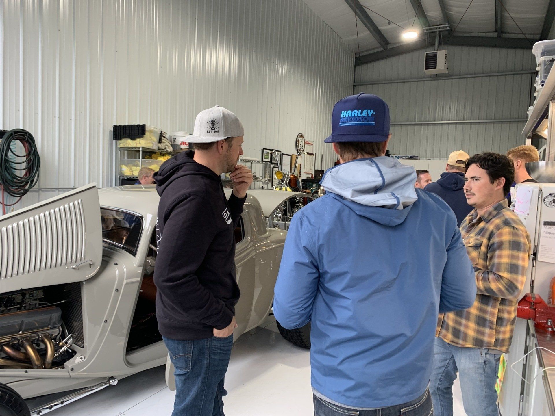 A group of men are standing around a car in a garage.