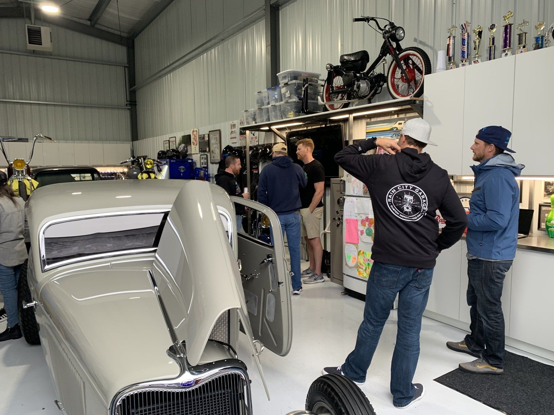 A group of people are standing around a car in a garage.