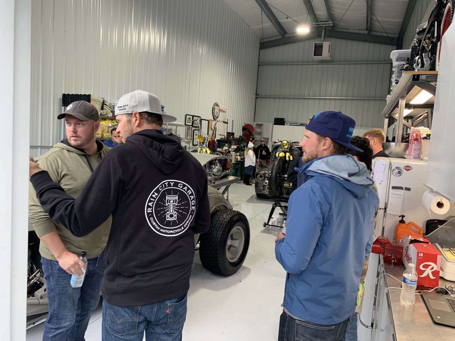A group of men are standing in a garage talking to each other.