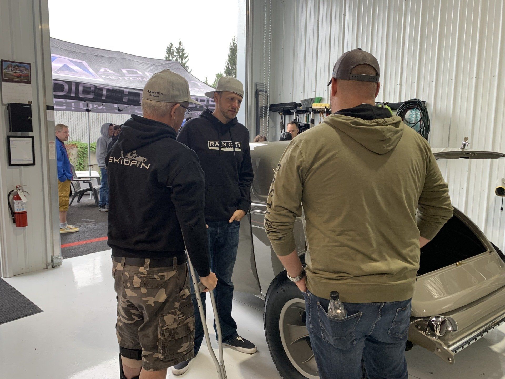 A group of men are standing around a car in a garage.