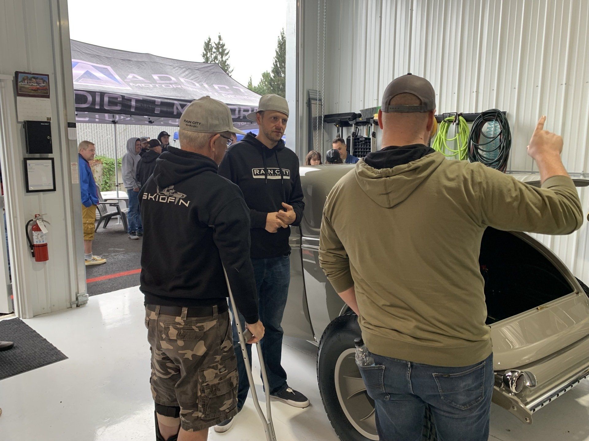 A group of men are standing around a car in a garage.