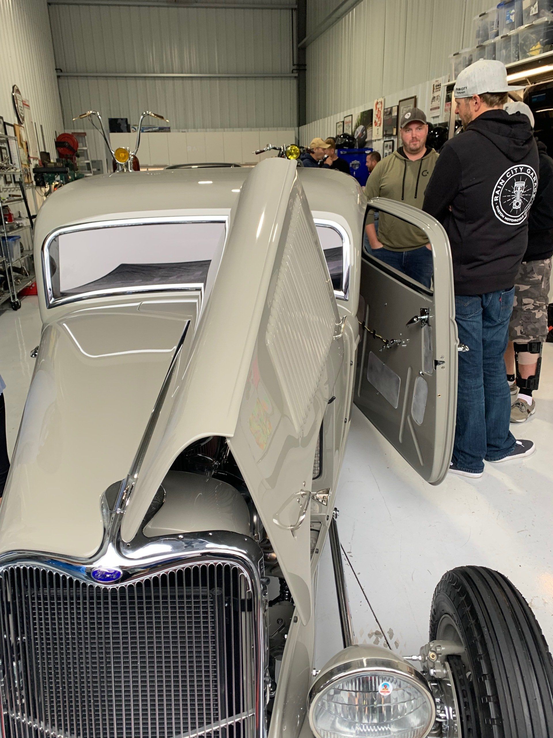 A group of men are standing around an old car in a garage.