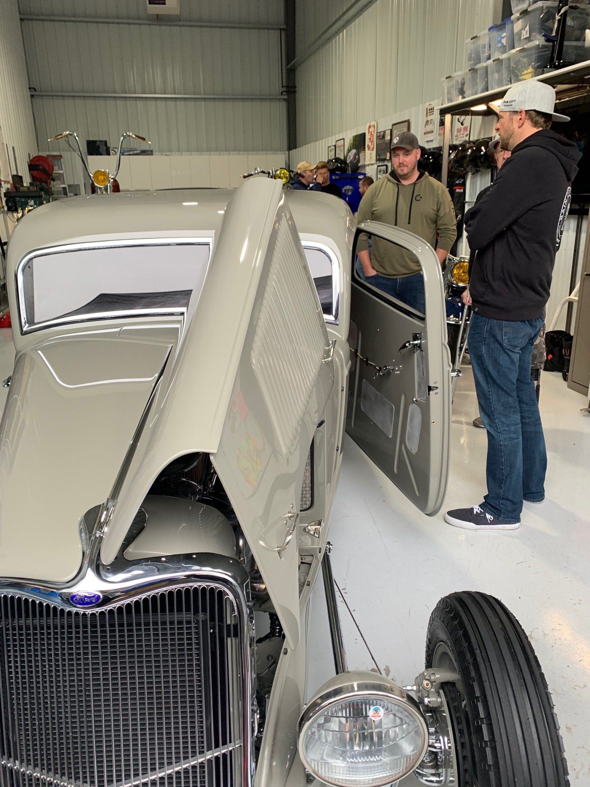 A group of men are standing around an old car in a garage.