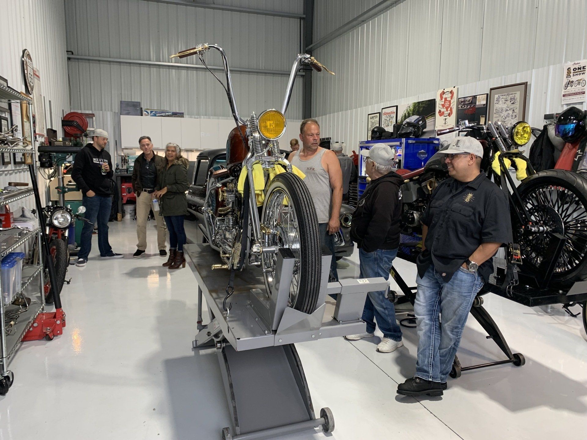 A group of people are standing around a motorcycle in a garage.