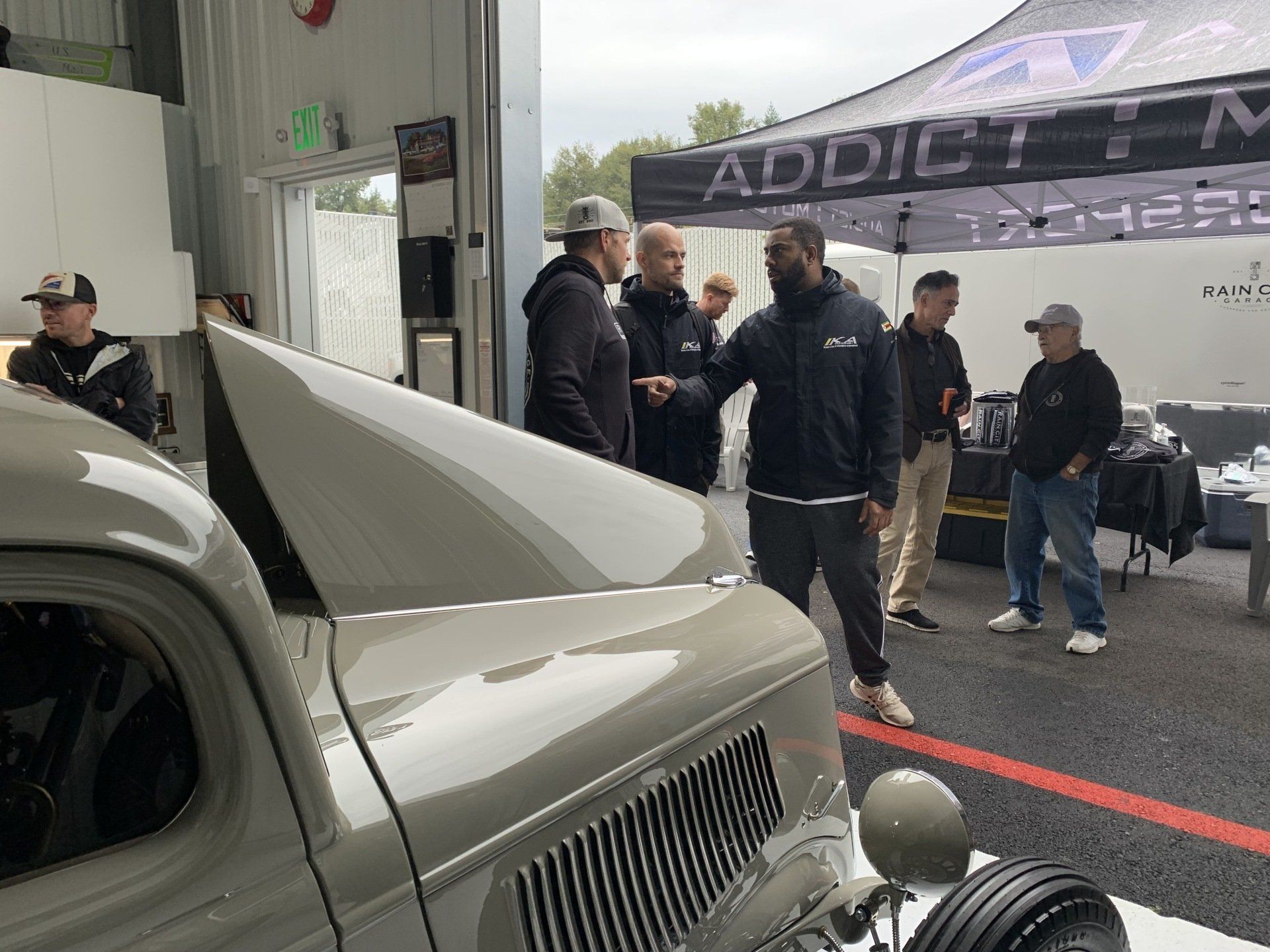 A group of men are standing around a car in a garage.