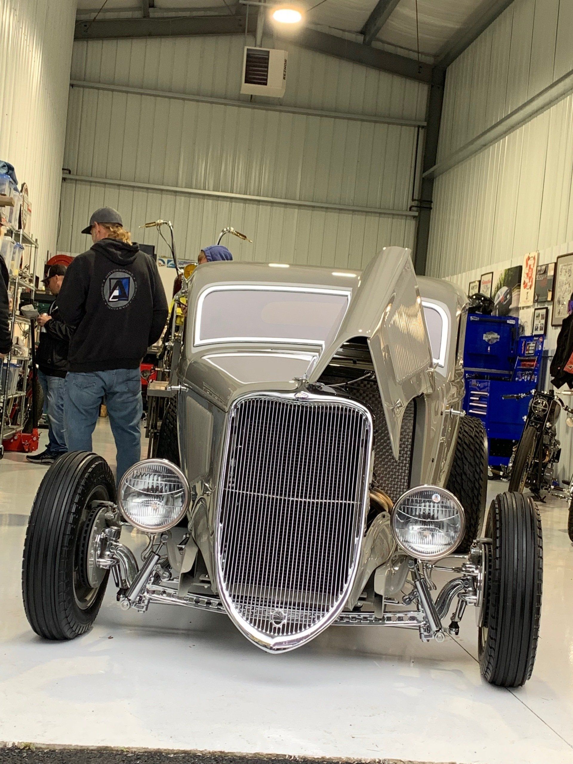 A man is standing next to a silver hot rod in a garage.