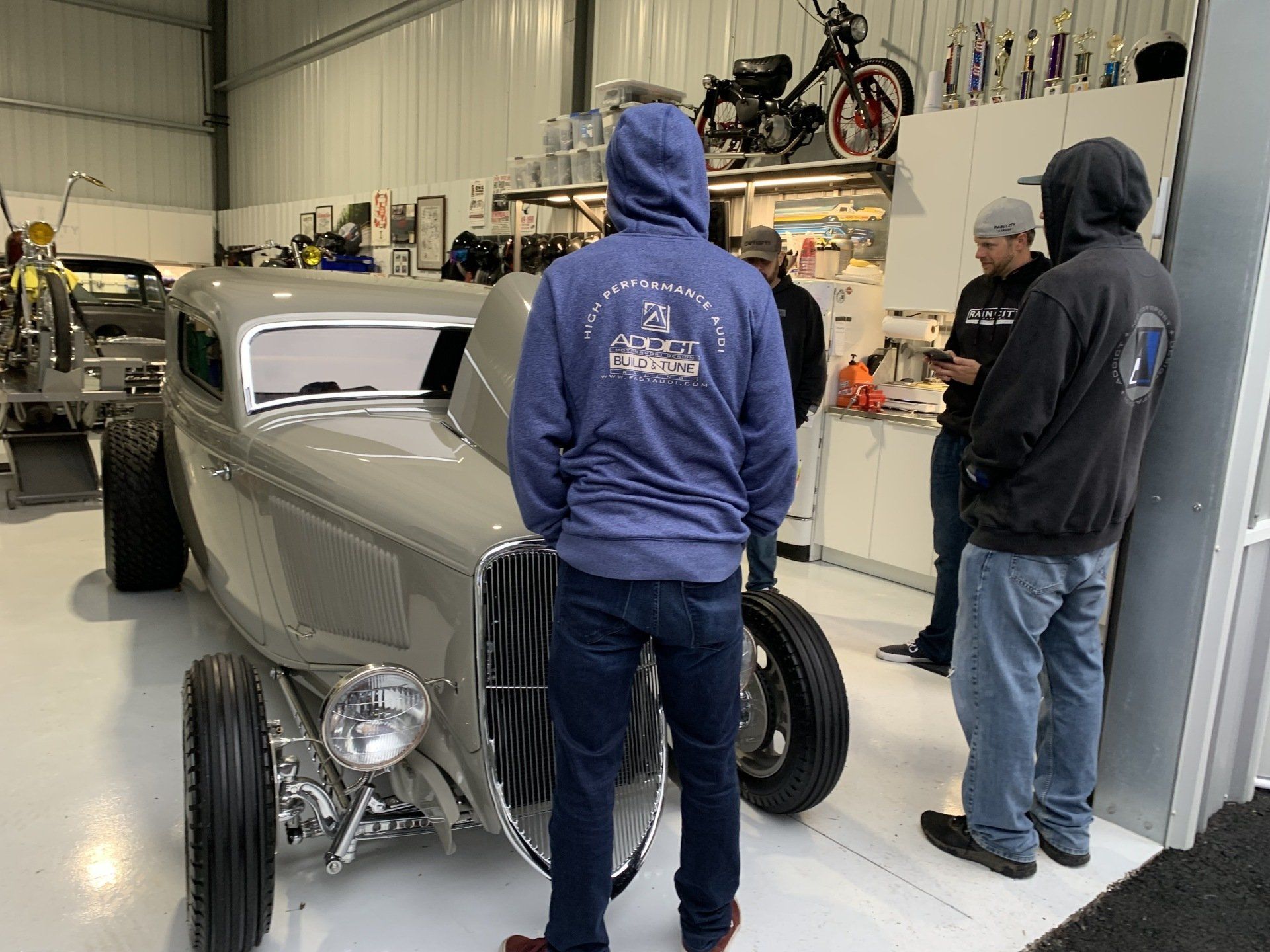A group of men are standing around a car in a garage.