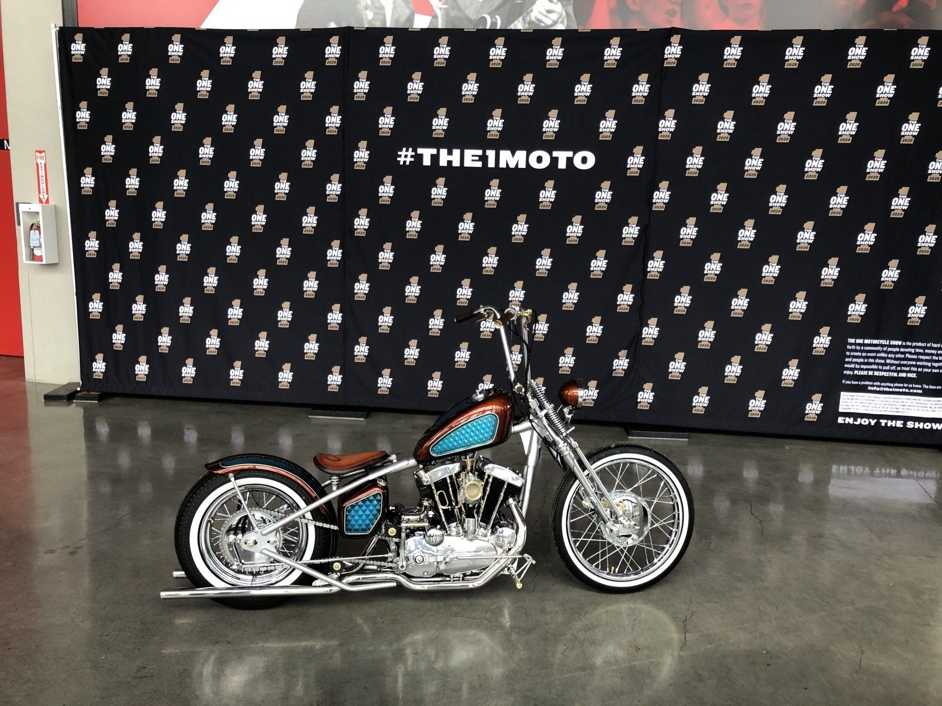 A motorcycle is parked in front of a wall that says #themoto