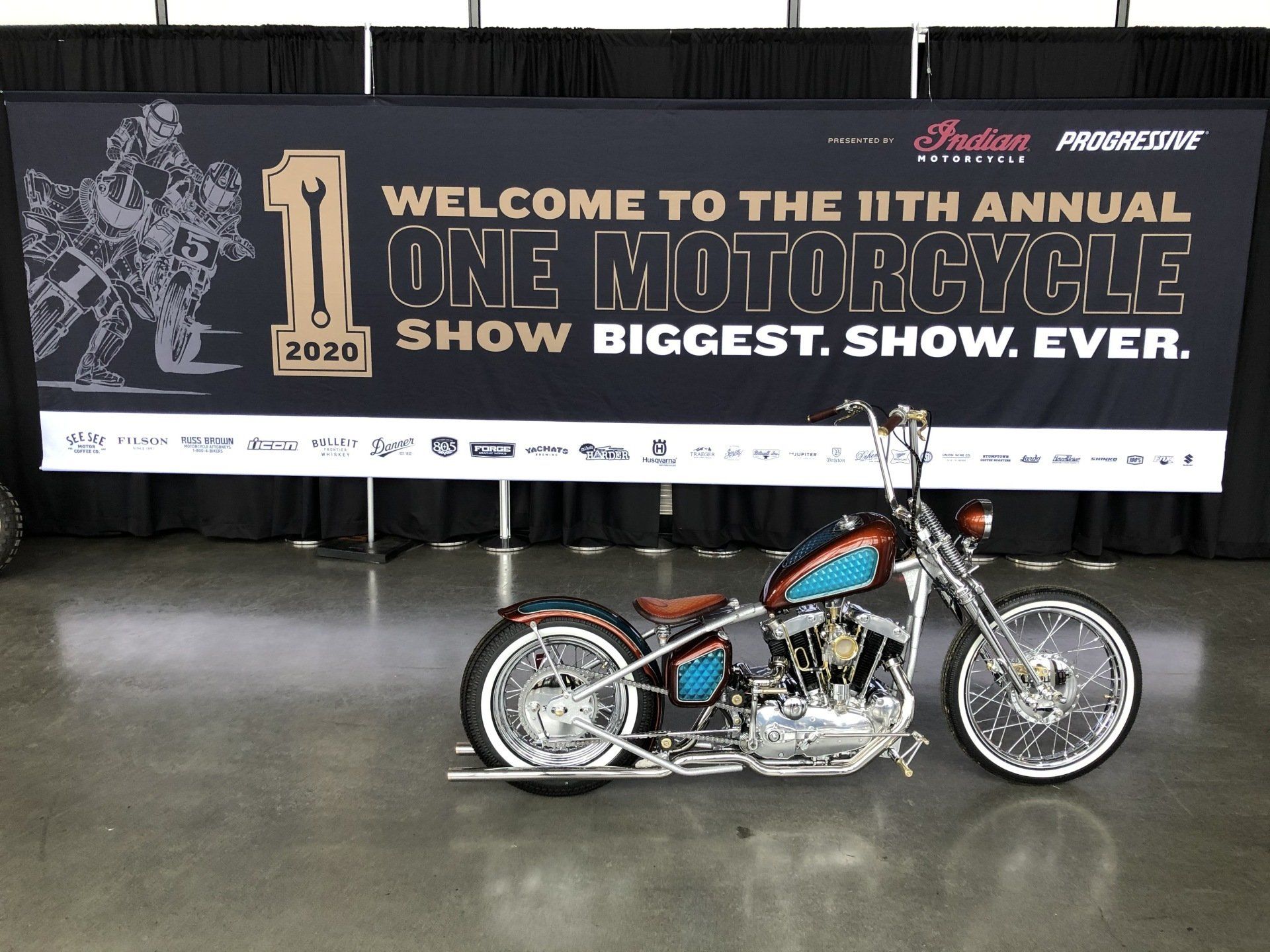 A motorcycle is parked in front of a sign that says welcome to the 11th annual one motorcycle show biggest show ever