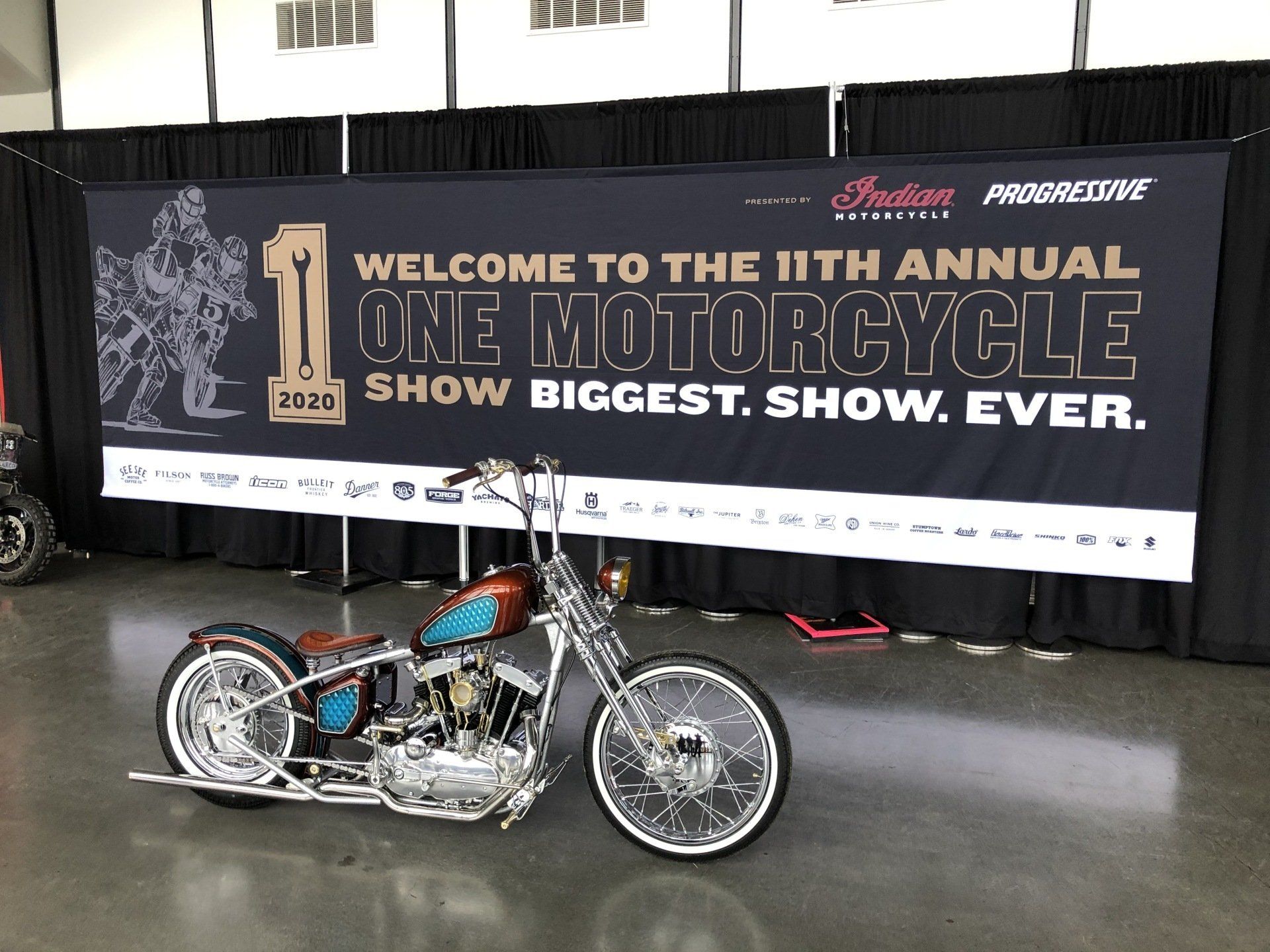 A motorcycle is parked in front of a sign that says welcome to the 11th annual one motorcycle show biggest show ever