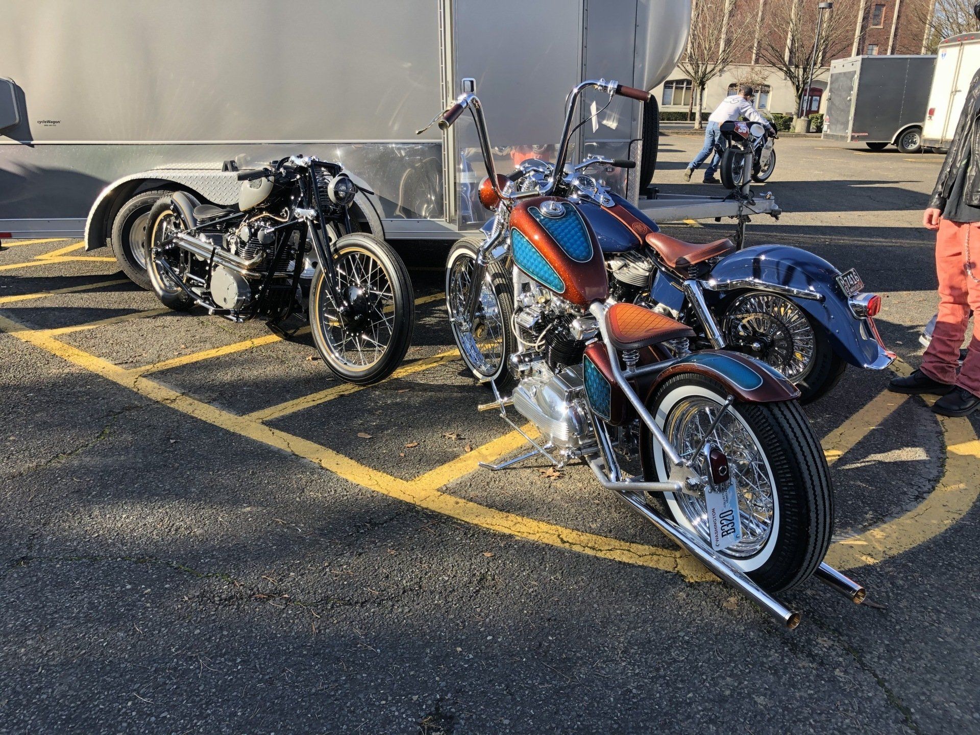 Three motorcycles are parked in a parking lot next to a trailer.