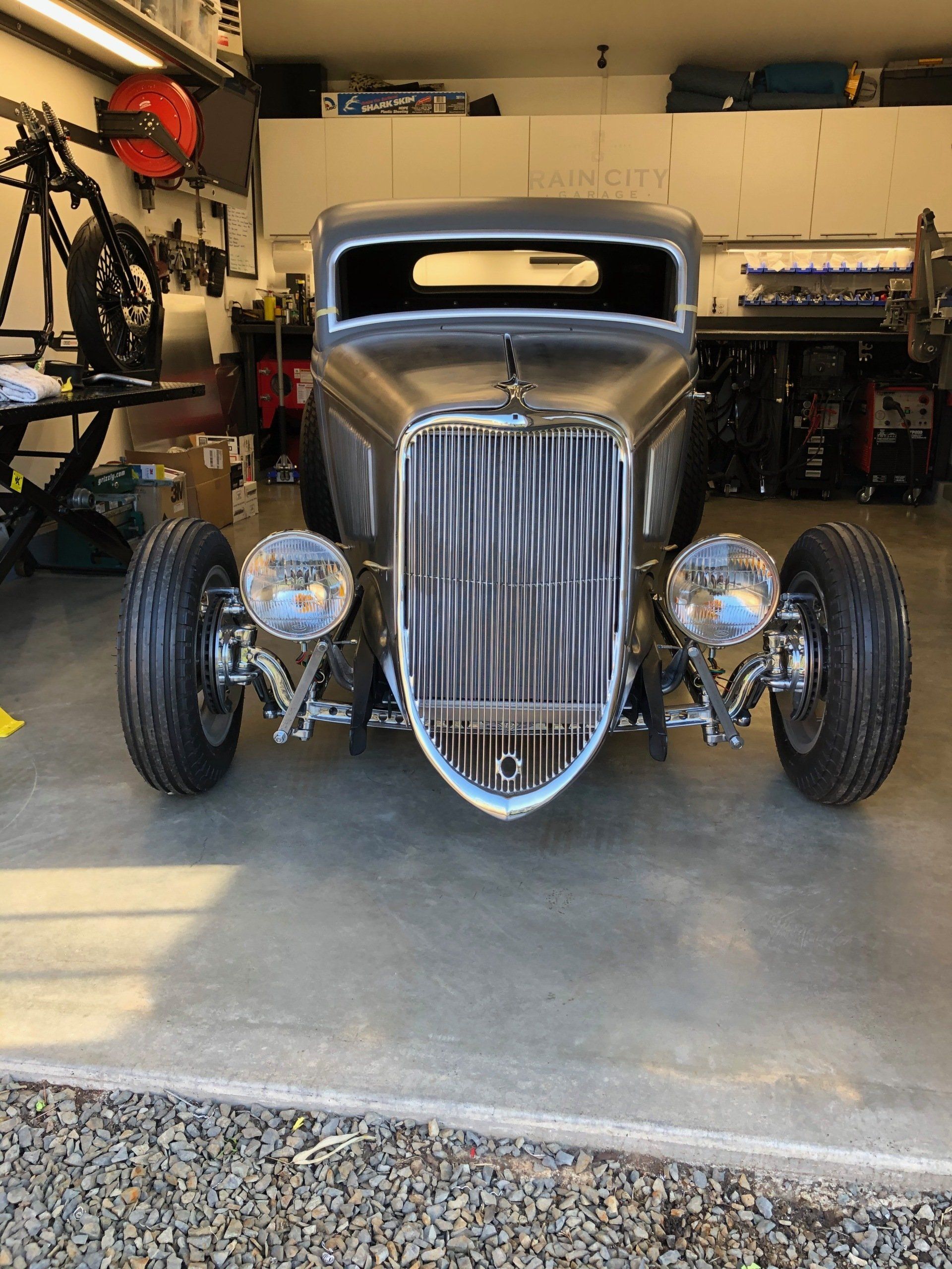 A hot rod is parked in a garage next to a motorcycle.