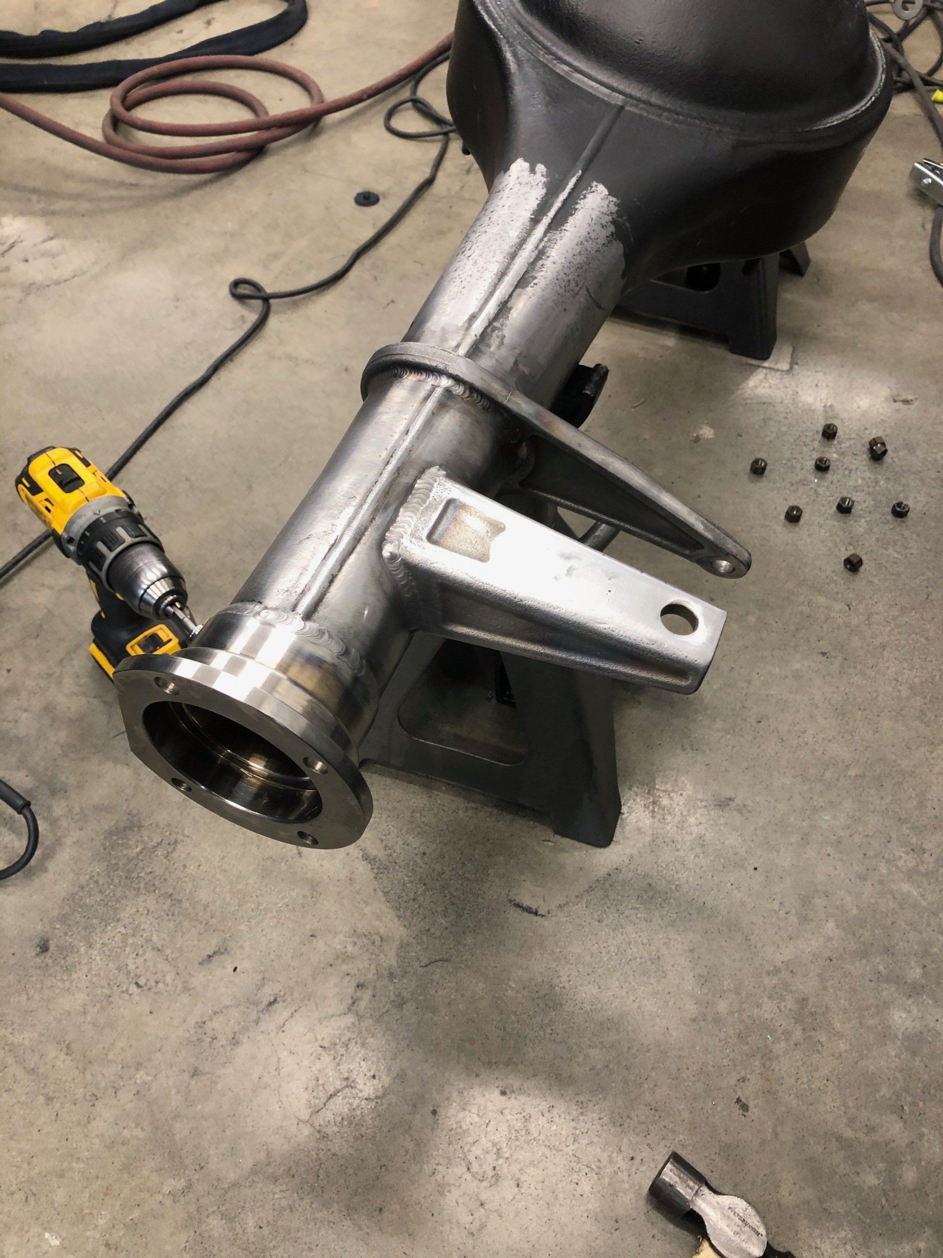 A metal pipe is sitting on a concrete floor next to a drill and pliers.