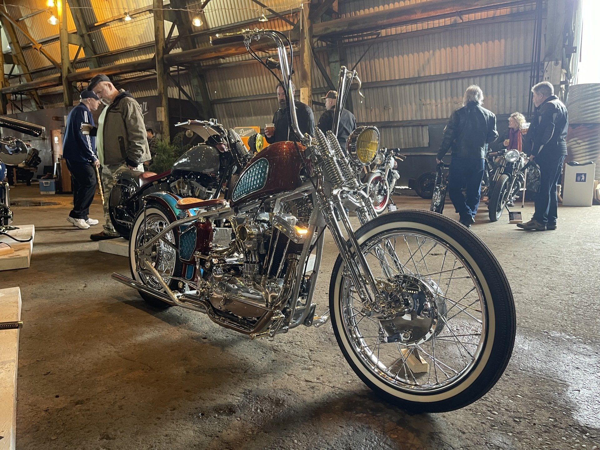 A motorcycle is parked in a garage with people standing around it.