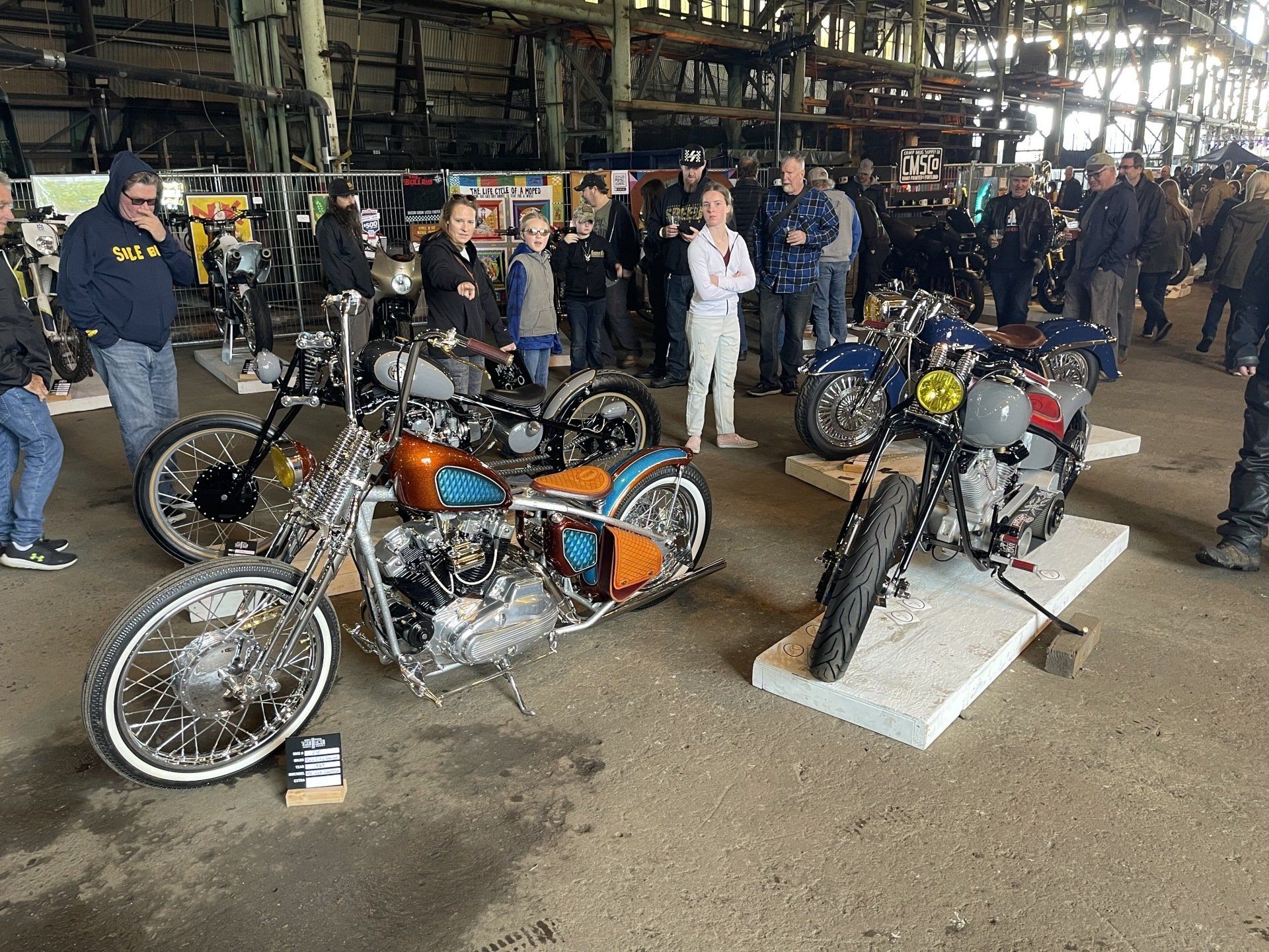 A group of people are standing around motorcycles in a warehouse.