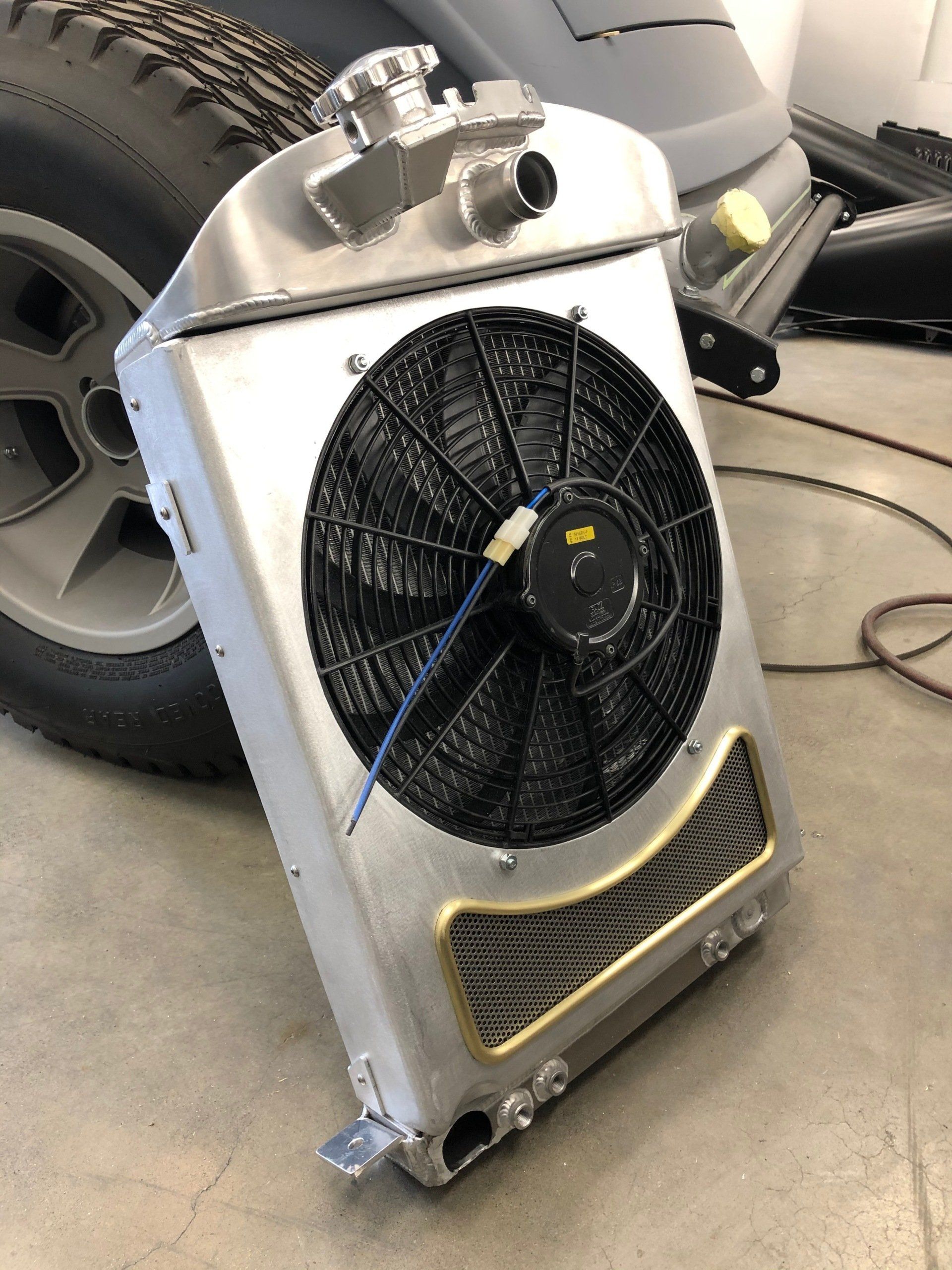 A radiator with a fan attached to it is sitting on the ground next to a tire.